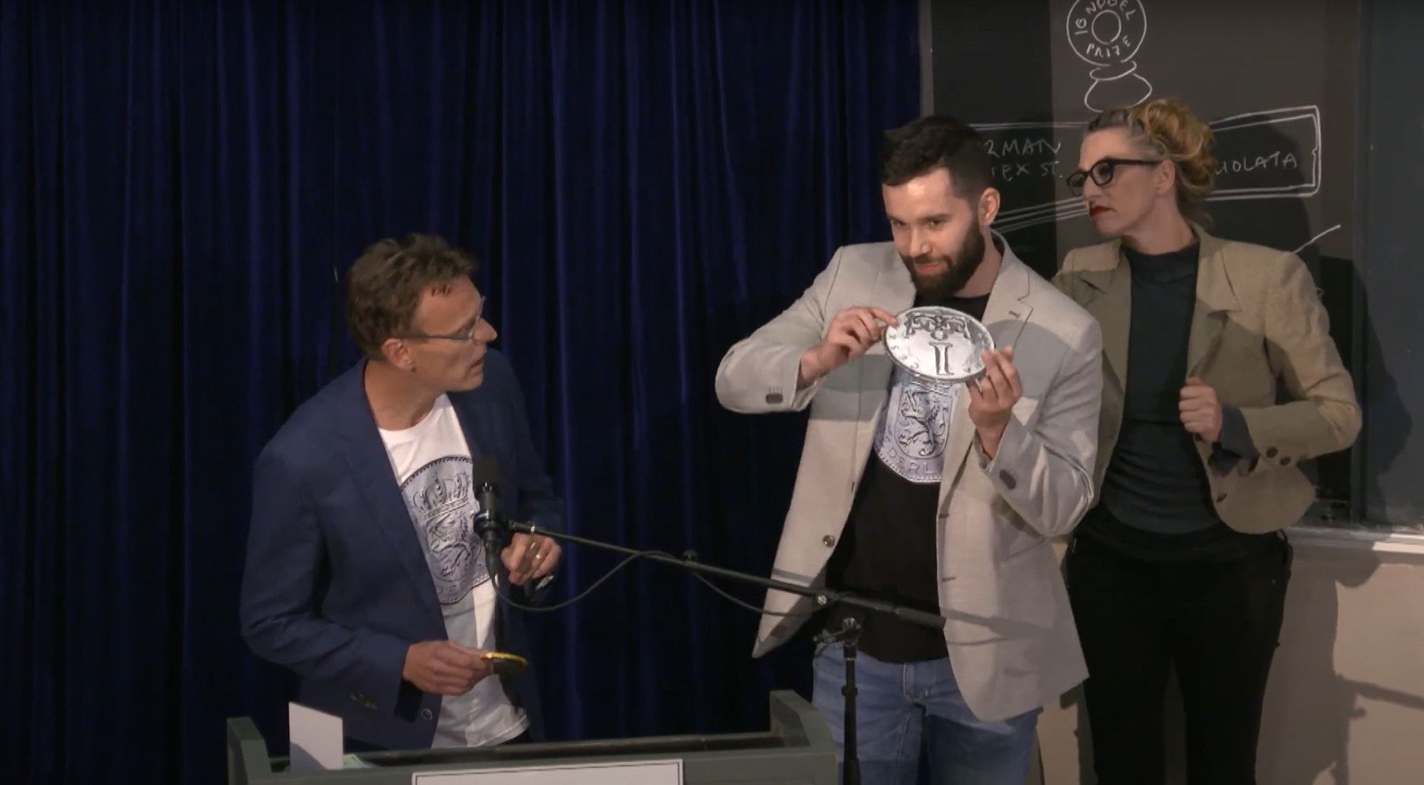 EJ and František explaining the findings on stage of the 2024 Ig Nobel Prize Ceremony. František has a large coin to demonstrate the physics behind the effect.