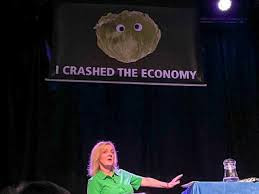 liz truss on stage underneath a huge picture of a lettuce with the text "I crashed the Economy"