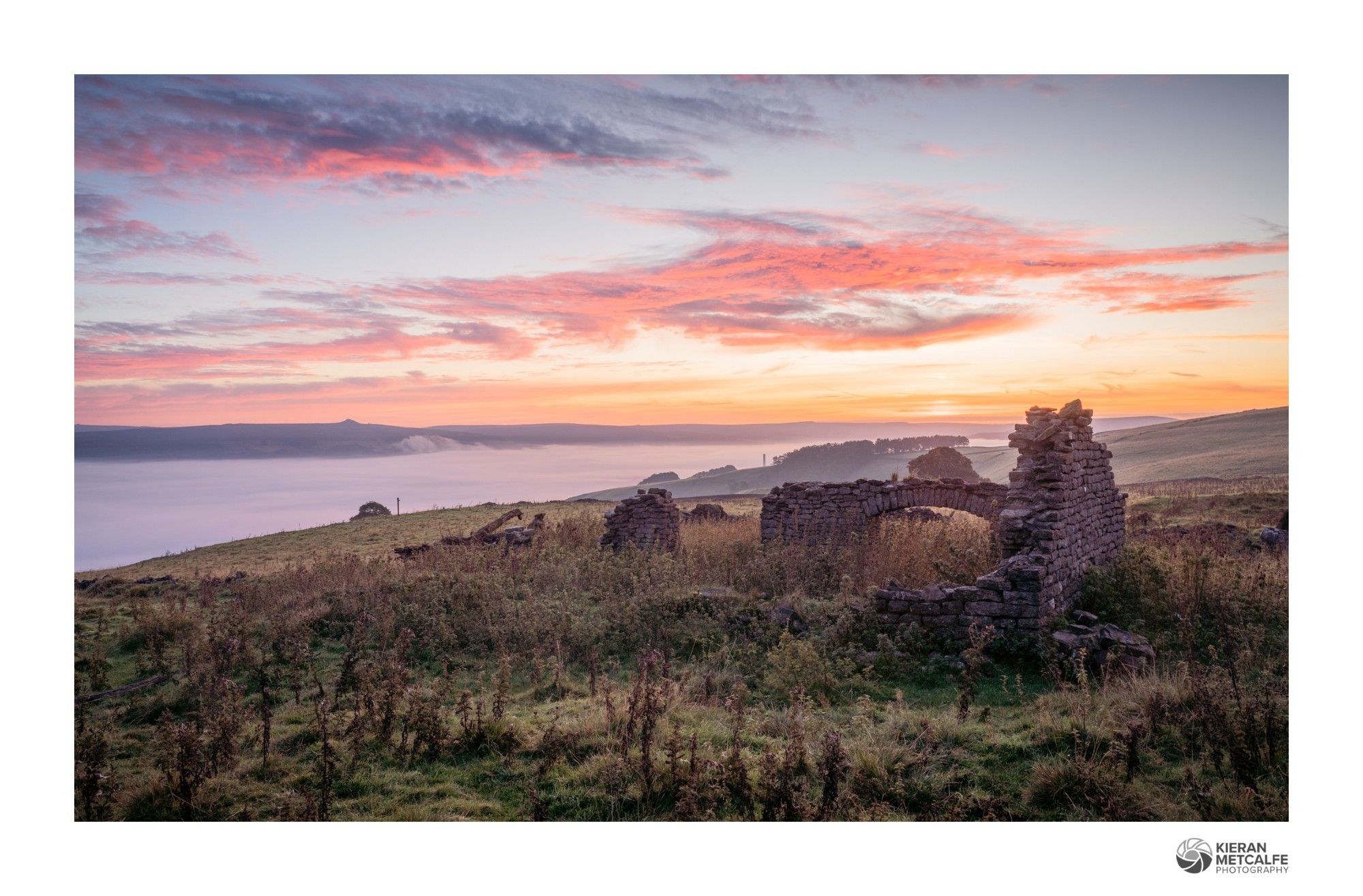 Sunrise at the remains of an old barn in the peak district. A cloud inversion is filling the valley in the background and the high clouds are vibrant pink.