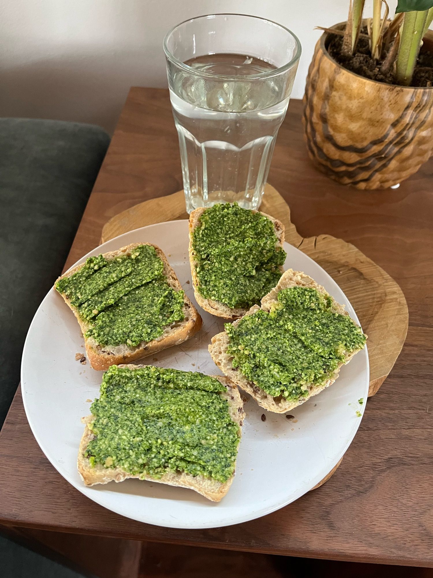 Twee mini broodjes opengesneden op een wit ontbijtbordje, besmeerd met knalgroene daslookpesto. Erachter staat een glas lichtgeel citroenwater.