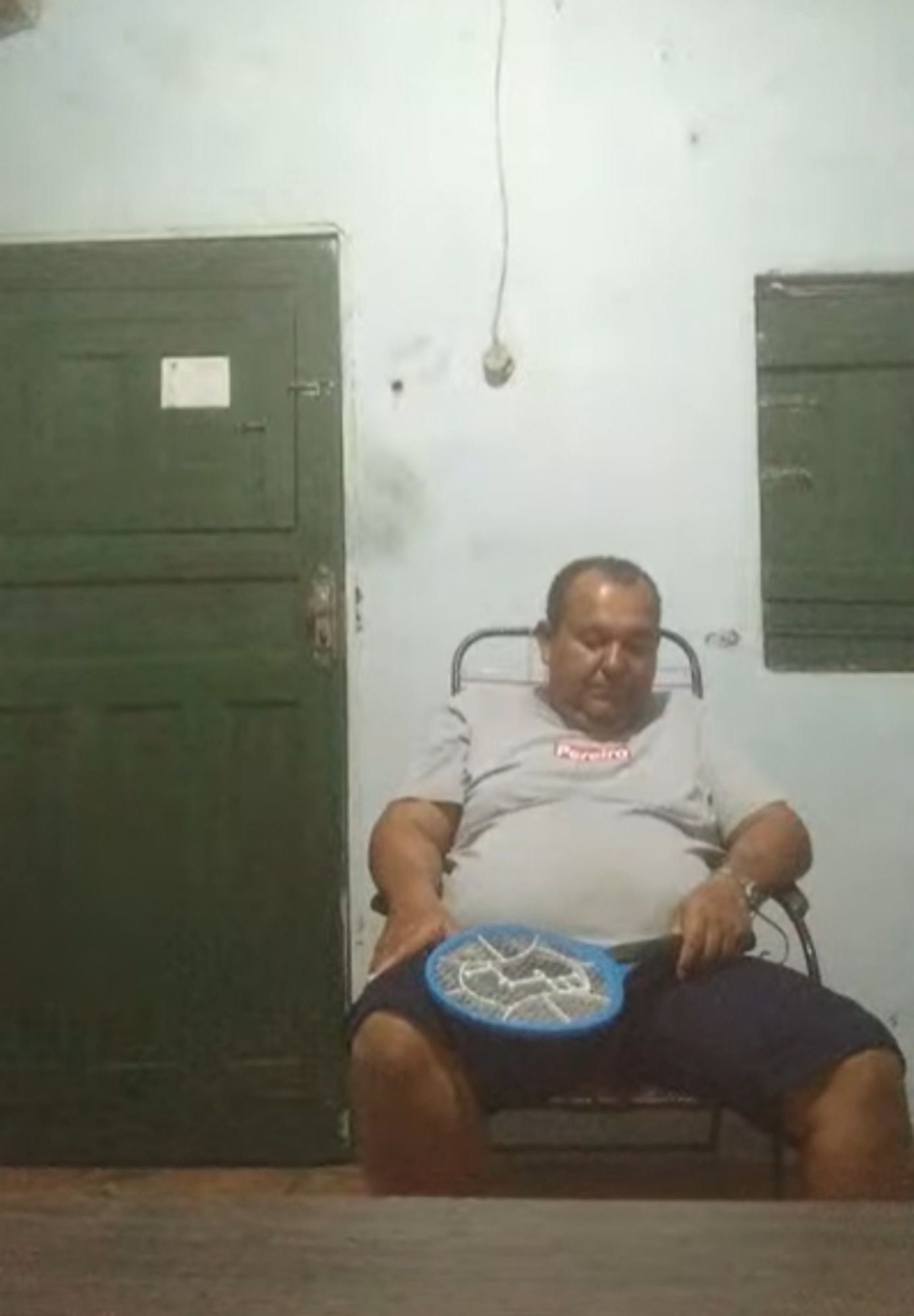 ednaldo pereira dormindo em uma cadeira segurando uma raquete de matar mosquito