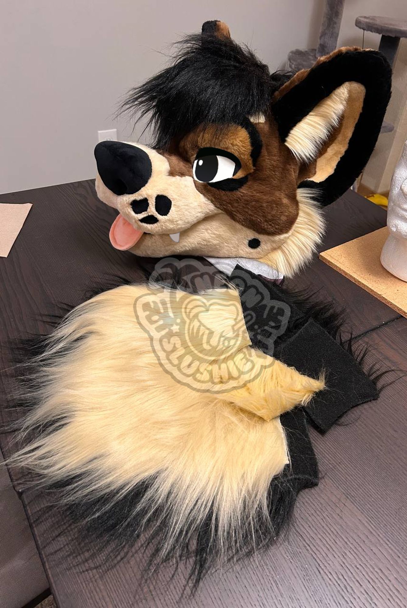 A photo of a brown dog fursuit head sitting on a table. Next to the head is the neck for the fursuit, broken down into pieces that haven't been sewn together yet. 🎨 🧵 #Fursuit #FurryArt #FurSale