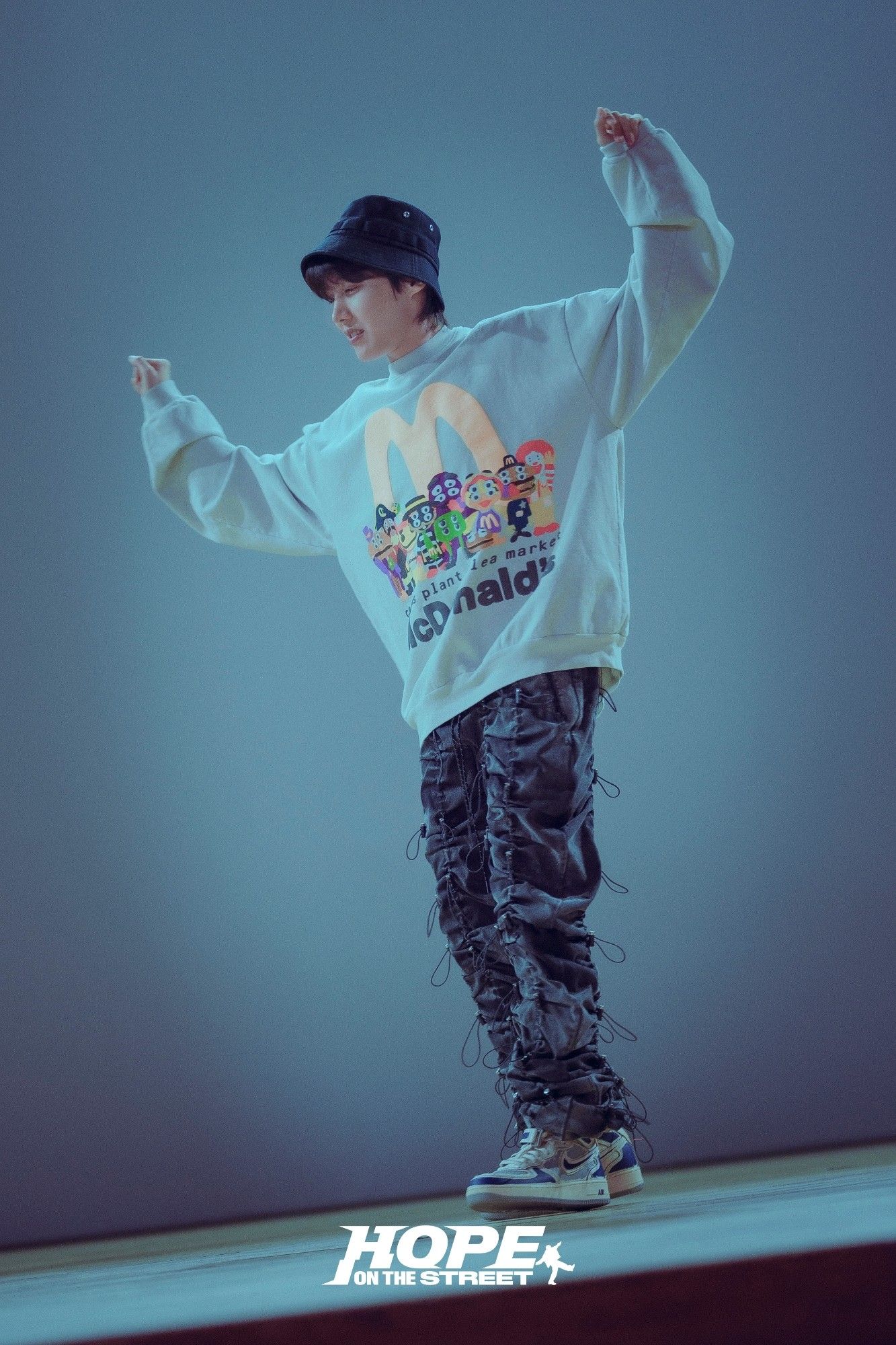 Photo of Hobi, wearing a oversized McDonald's pullover, jeans and is dancing.