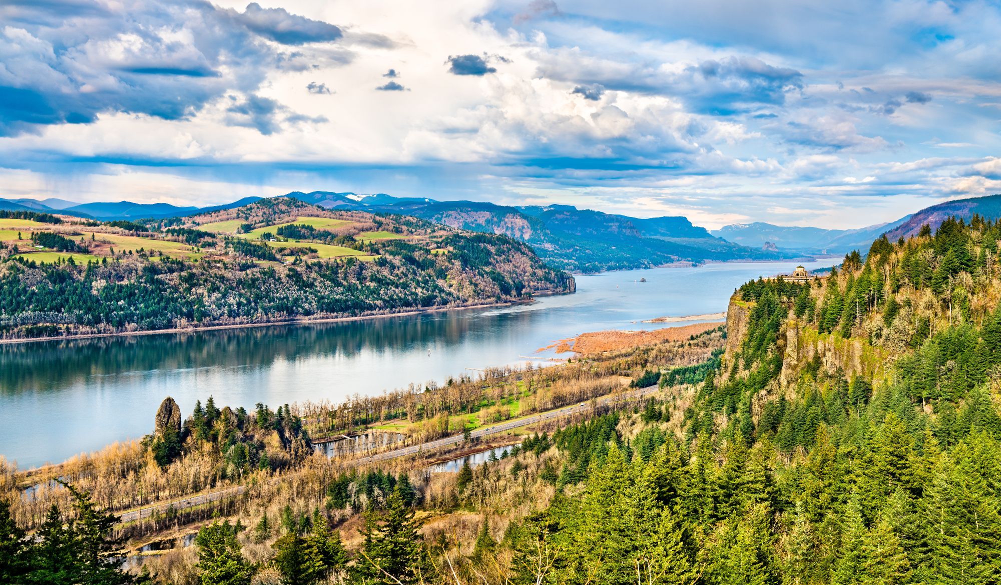 The Columbia River (US) flowing through a valley between two rocky ridges, with forest in the foreground and pasture in the background