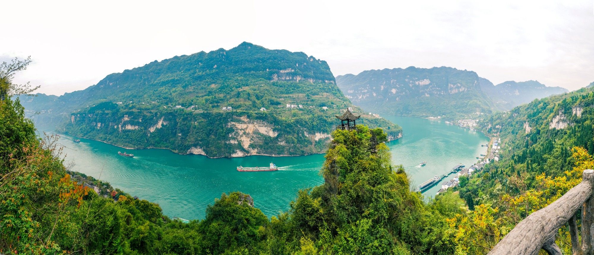 The Yangtze River (China) curving through a valley between two steep mountains. The water is very green and the mountains are covered in trees and light mist