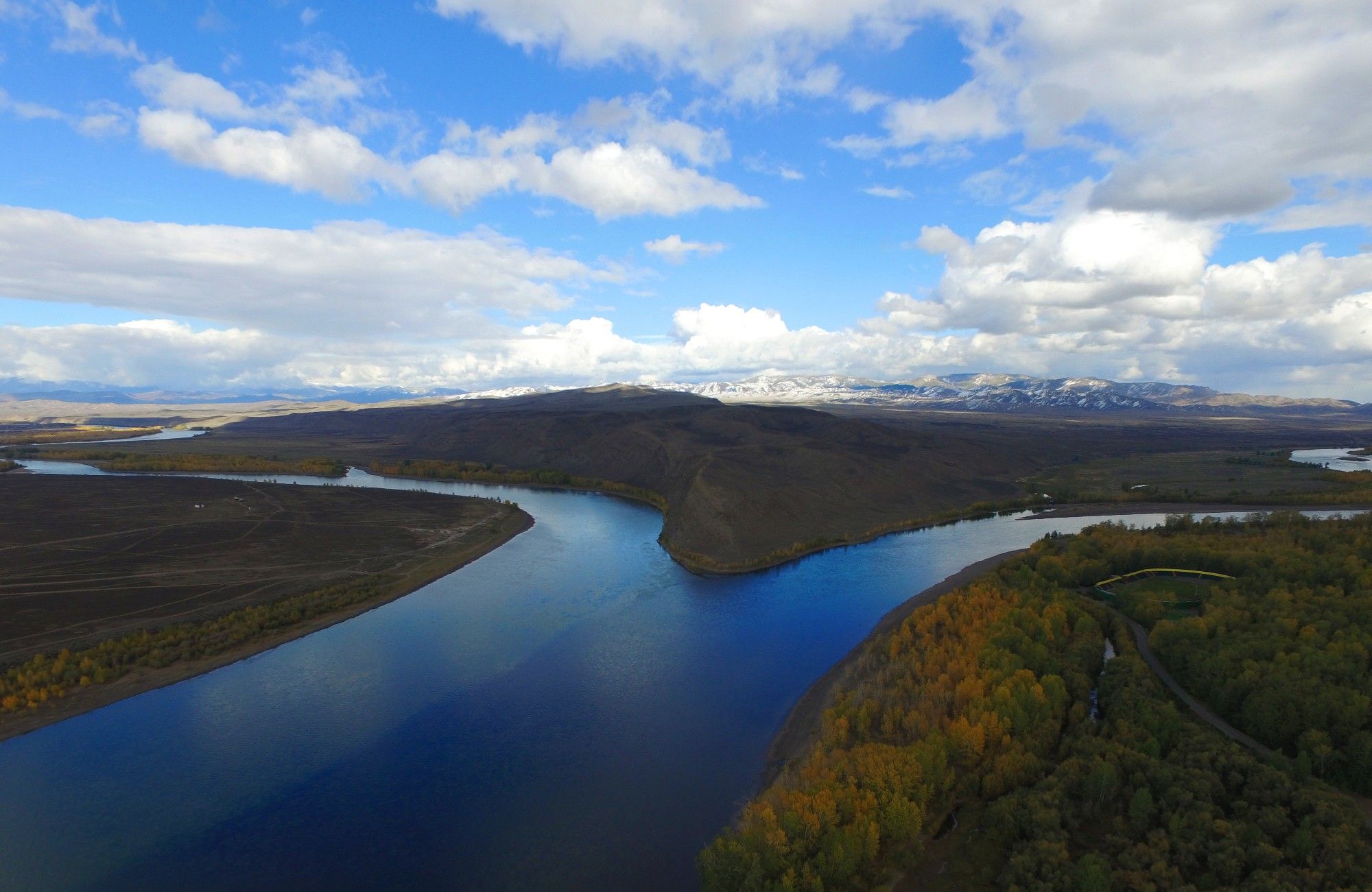 two tributaries of the Yenisey river coming together, with dense forests on the river banks and a large mountain range in the background