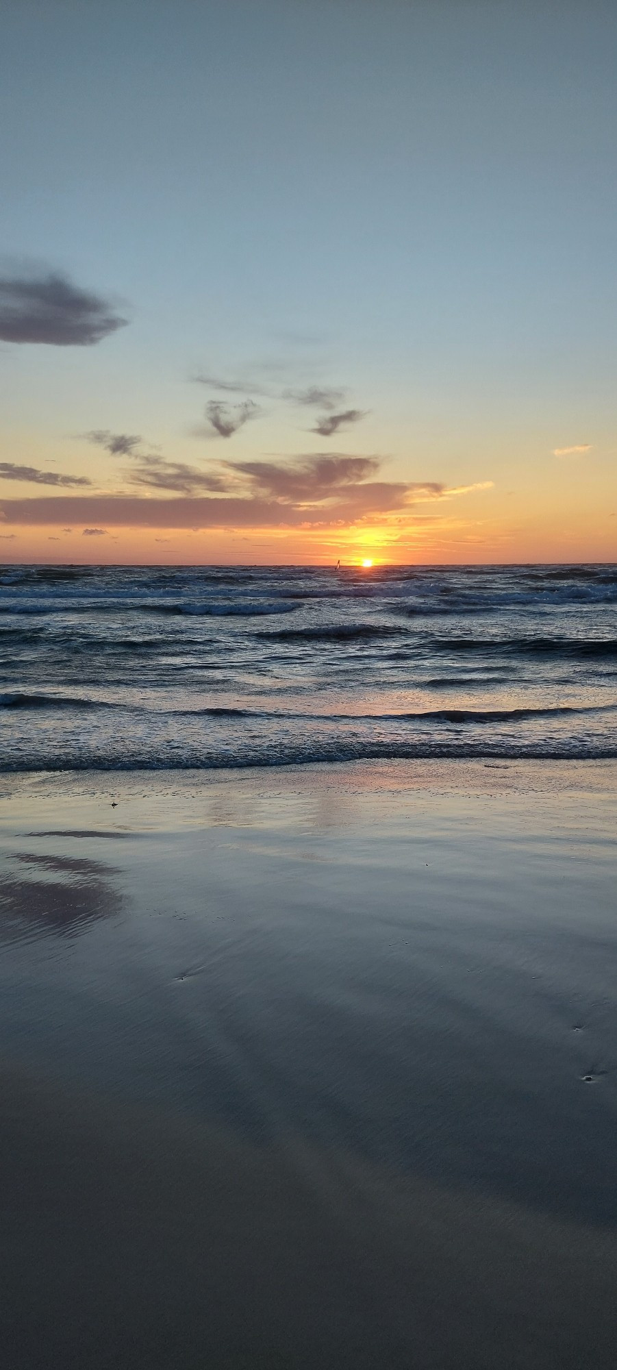 Bewegtes Meer, glatter nasser Sand, Sonnenuntergang mit wenigen kleinen Wölkchen