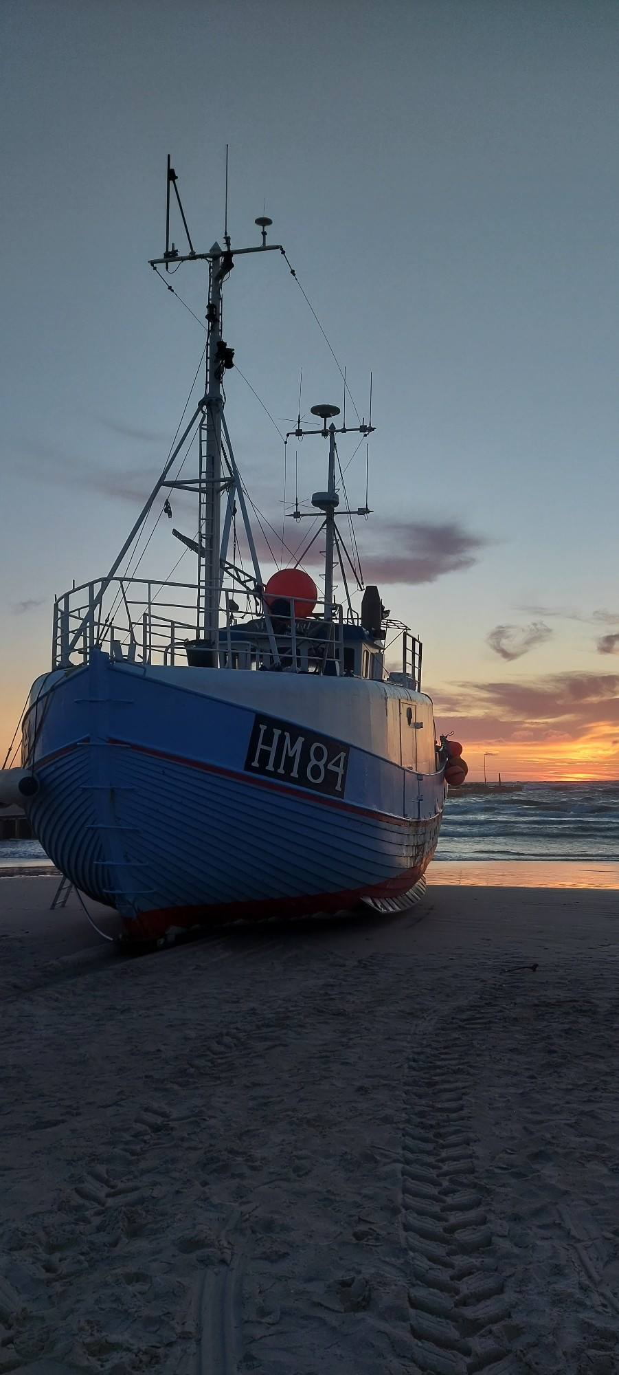 Ein Fischerboot liegt auf den Strand von Løkken hochgezogen vor dem Sonnenuntergang