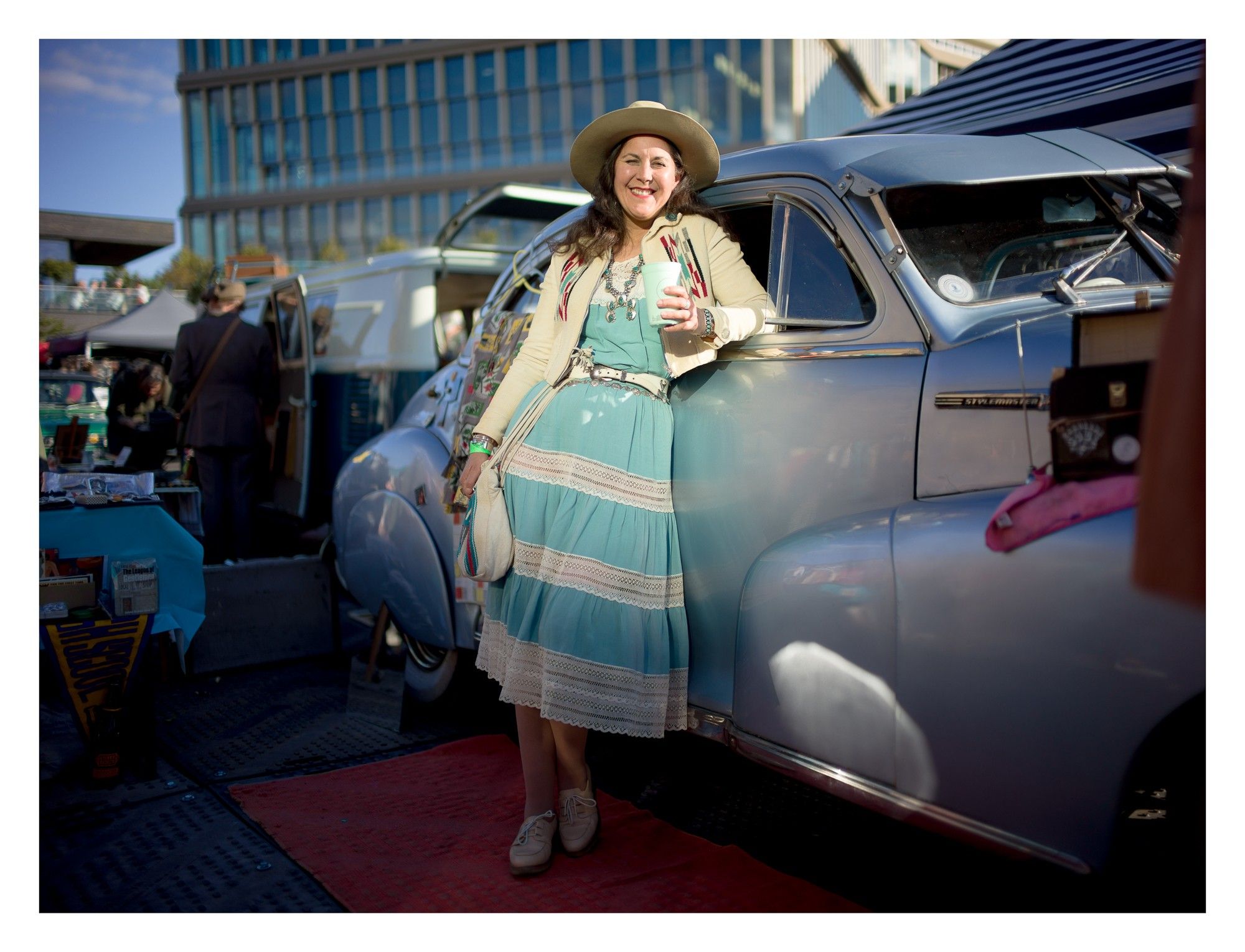 Portrait of a woman in vintage clothing leaning on a classic car.