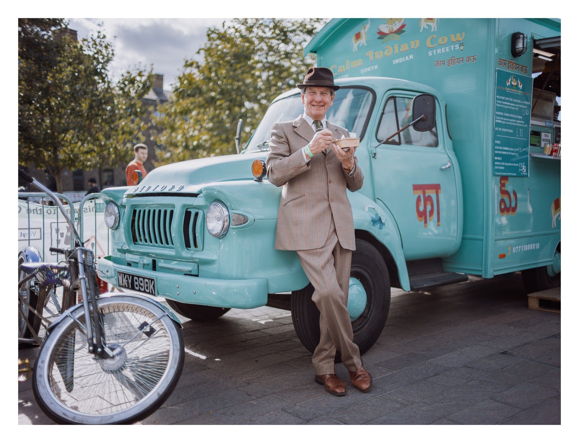 Portrait of a man in vintage clothing leaning on a classic food truck.