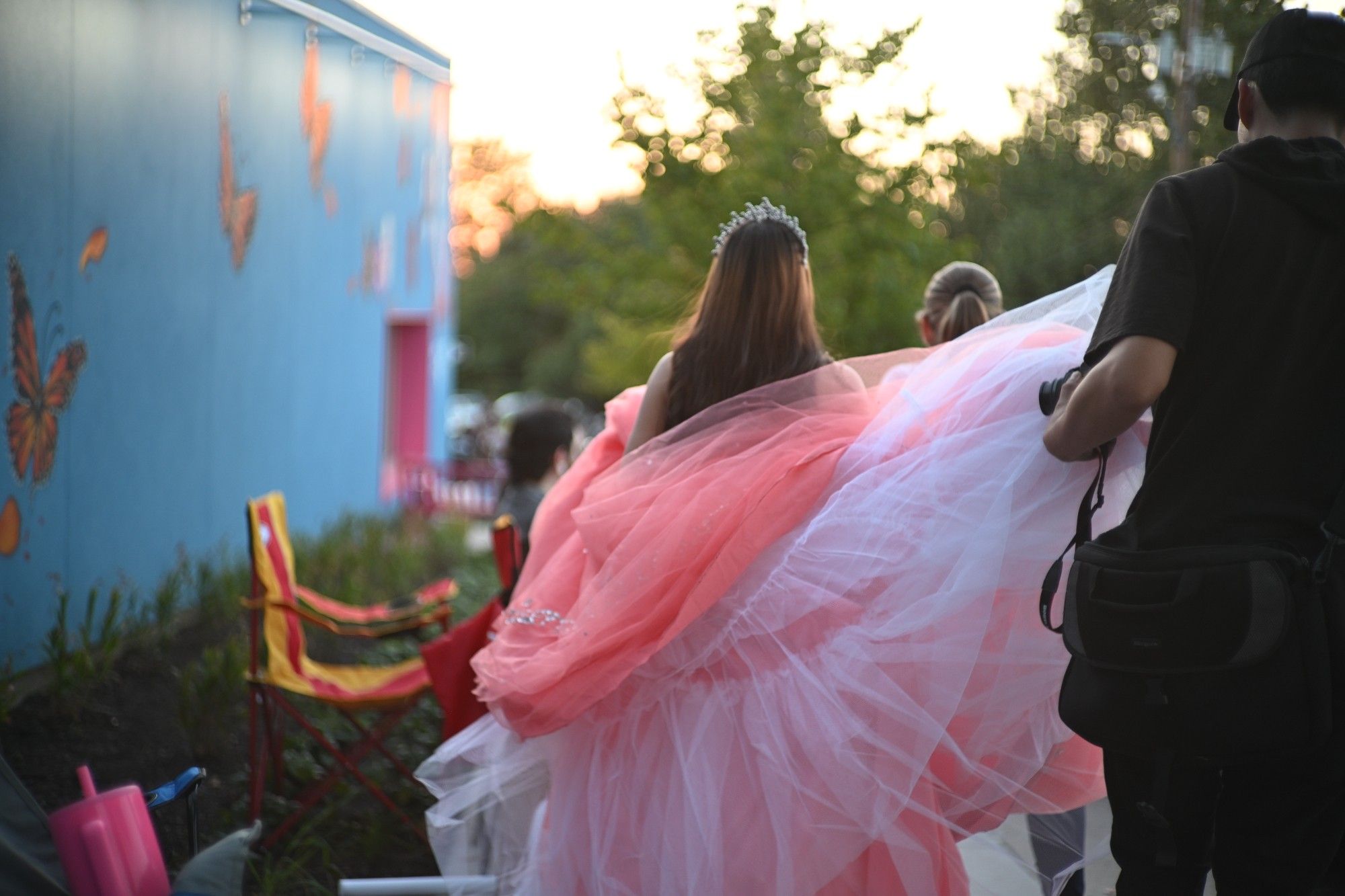 A girl wearing a pink dress being trailed by a pro photographer in the standard goth uniform of his kind