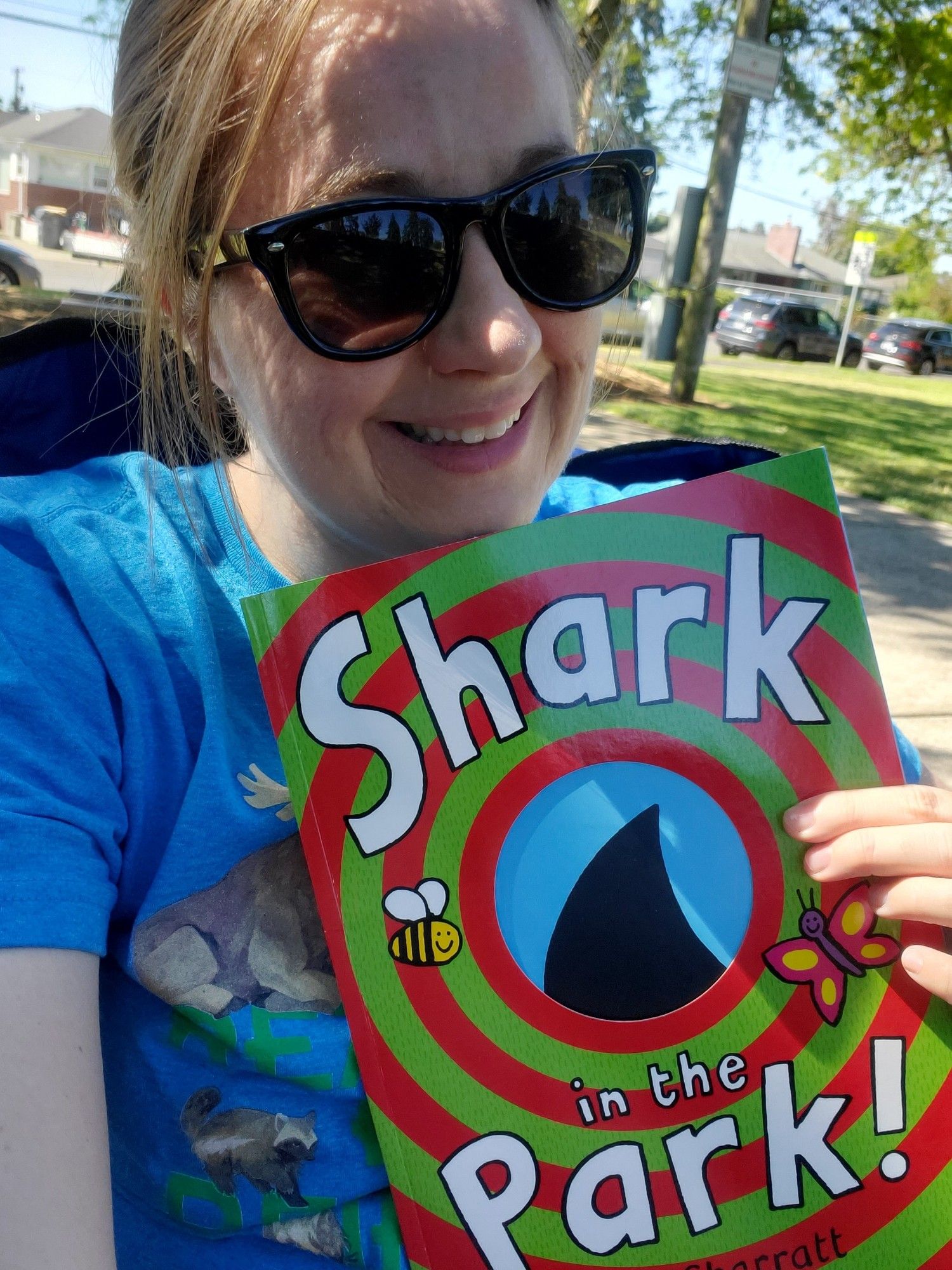 Jessica, sporting sunglasses and a ponytail, displays the picture book Shark In the Park!