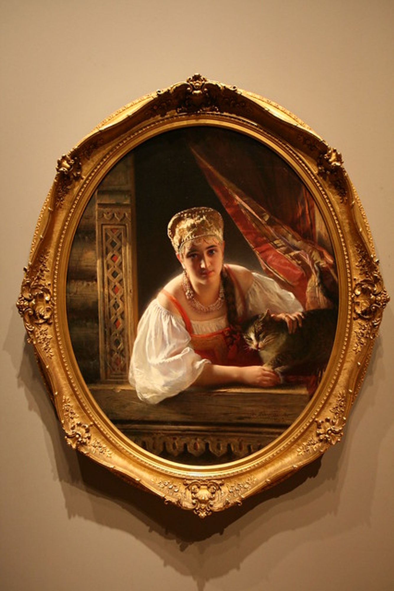 The painting "Russian Beauty with Cat", showing a woman in a window, bathed in sunlight, petting a cat that is snuggling against her. It has an ornate frame somewhat resembling a giant cameo pendant