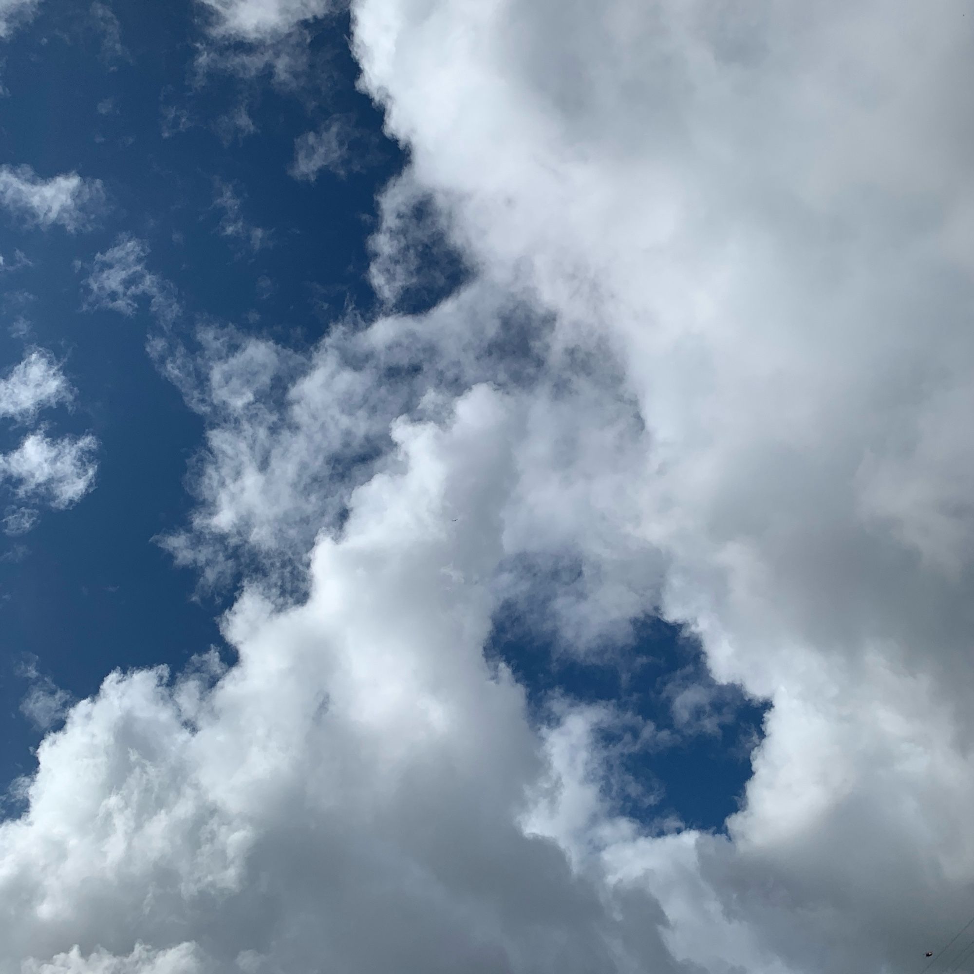 A large cloud formation over a clear blue sky, with a hole in the main cloud, through which you can see the sky behind.