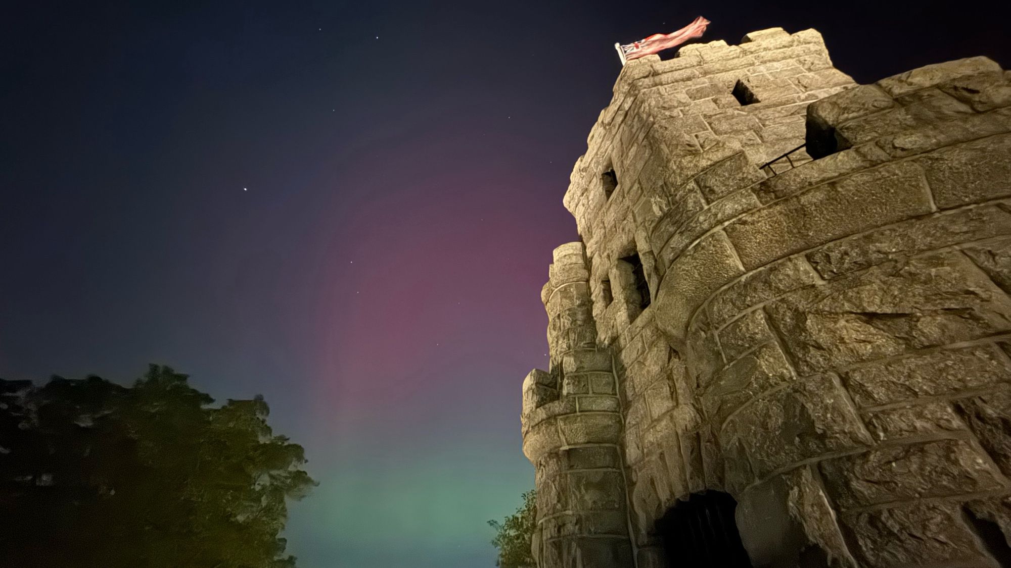 Pink and green aurora behind big ol’ castle-looking monument.