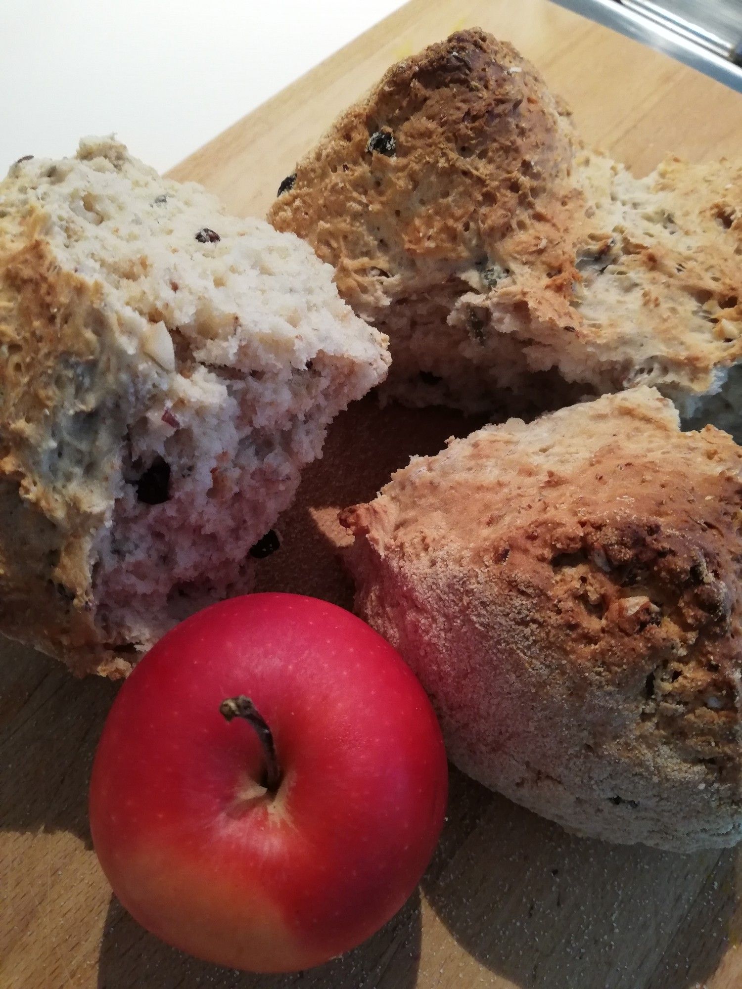 Round of Irish soda bread, broken into quarters on a bread board, along with a bright red apple