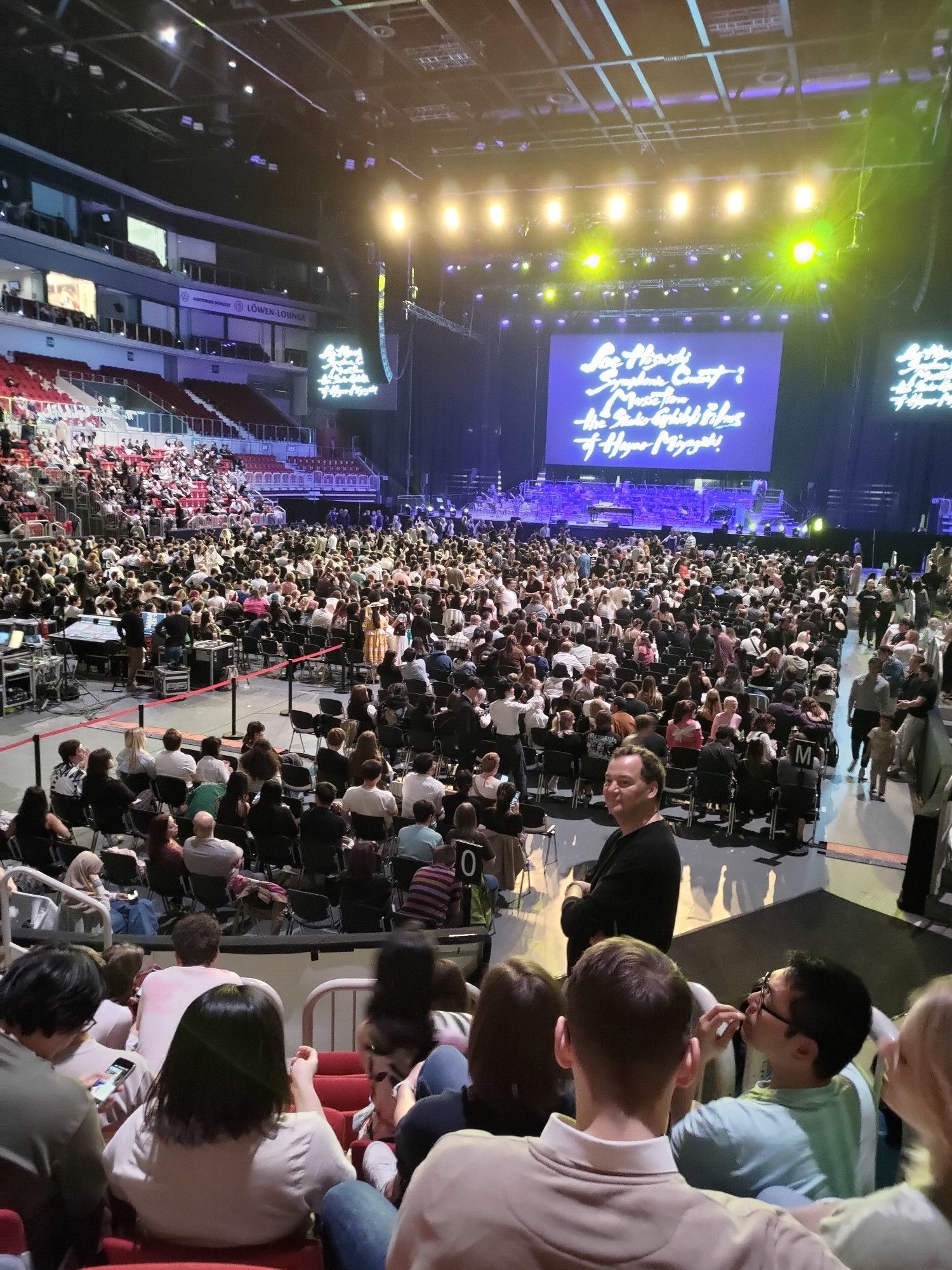 Een gevulde concertzaal met op het scherm de woorden 'Joe Hisaishi Symphony Concert: Music from the Studio Ghibli films from Hayao Miyazaki'