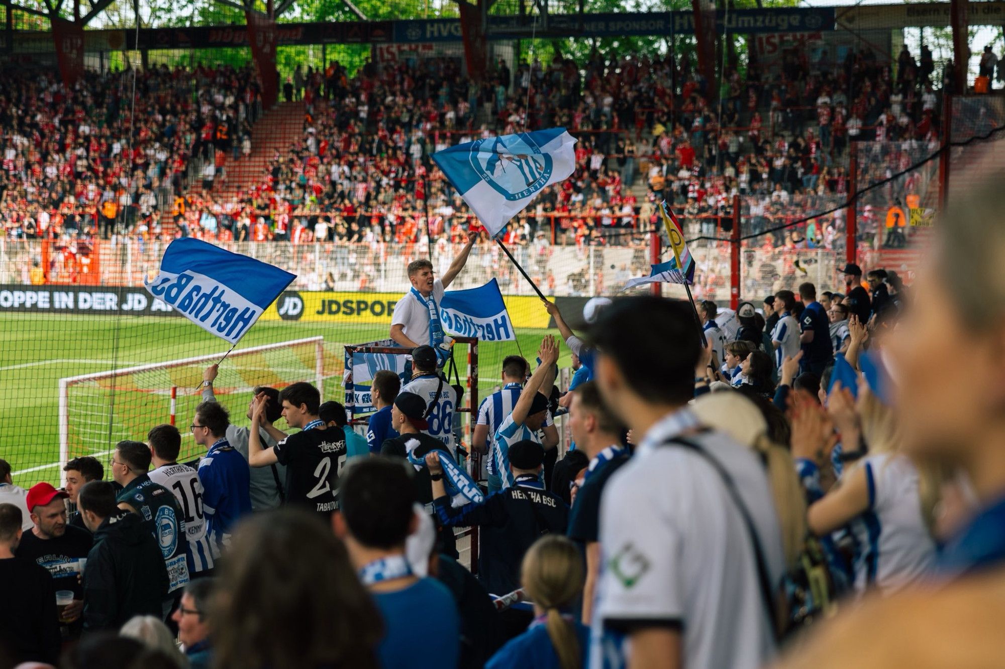 Blick im Auswärtsblock. Mit Fans, die Herthafahnen schwenken und dem Capo, der alle anfeuert