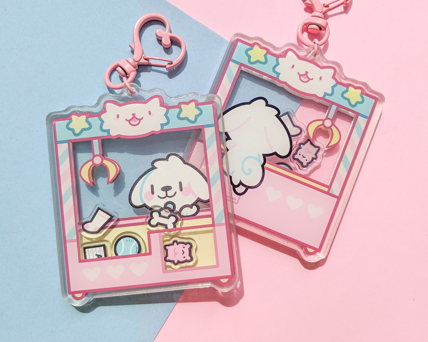 Acrylic shaker charm of a white puppy at a UFO catcher machine.  The shakable pieces inside the machine are of a sock, bear plushie, bone, tennis ball, and homework.  The charm is on a blue and pin background.