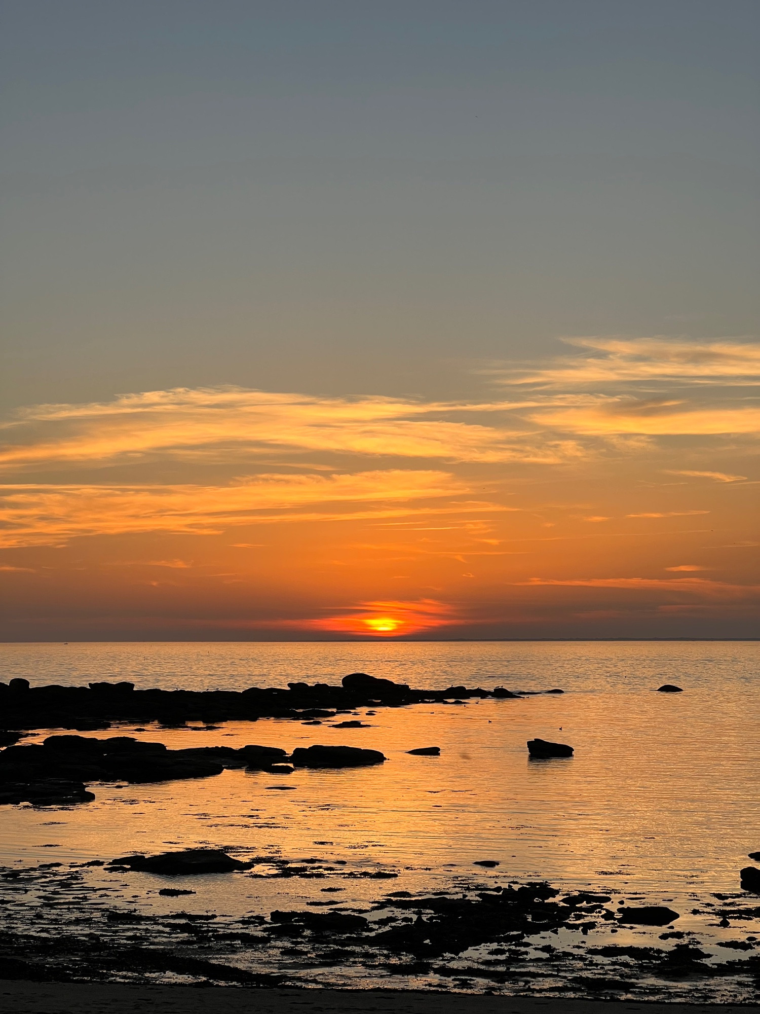 Coucher de soleil sur la mer, on voit des rochers et la mer est orange avec les reflets