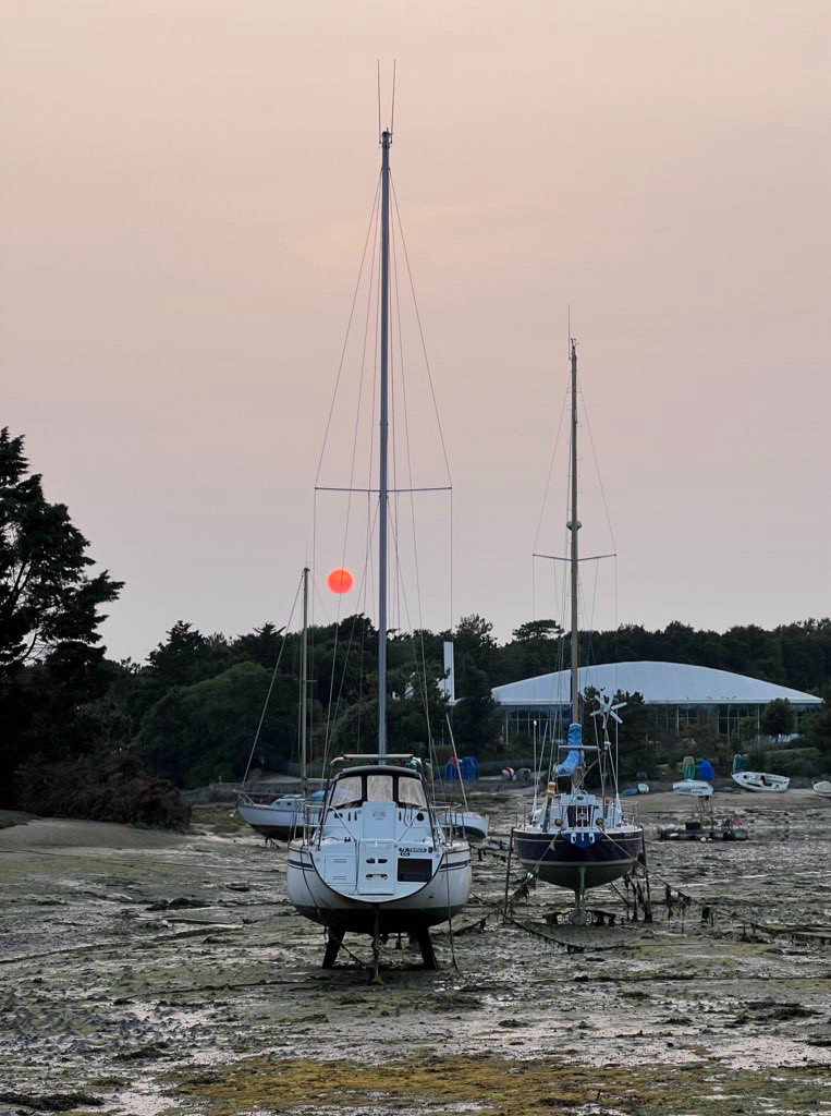 Soleil rouge voilé visible derrière les voiliers