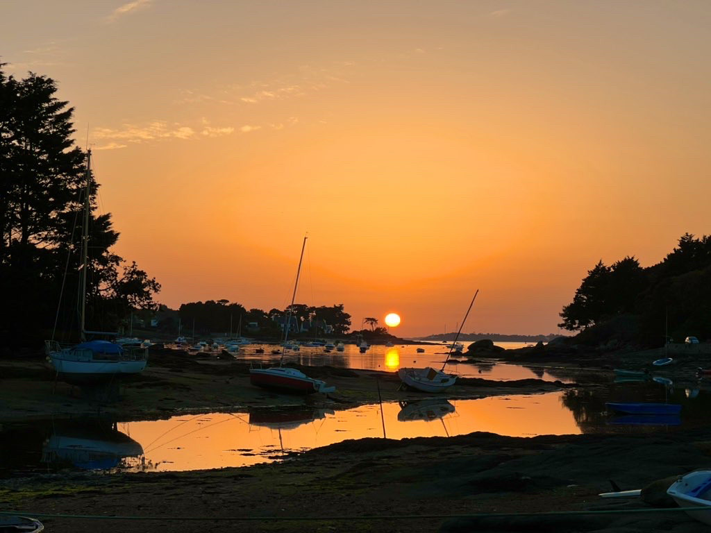 Coucher du soleil sur la ria, au bout de la rue, le ciel est orangé, le soleil se reflète sur la mer