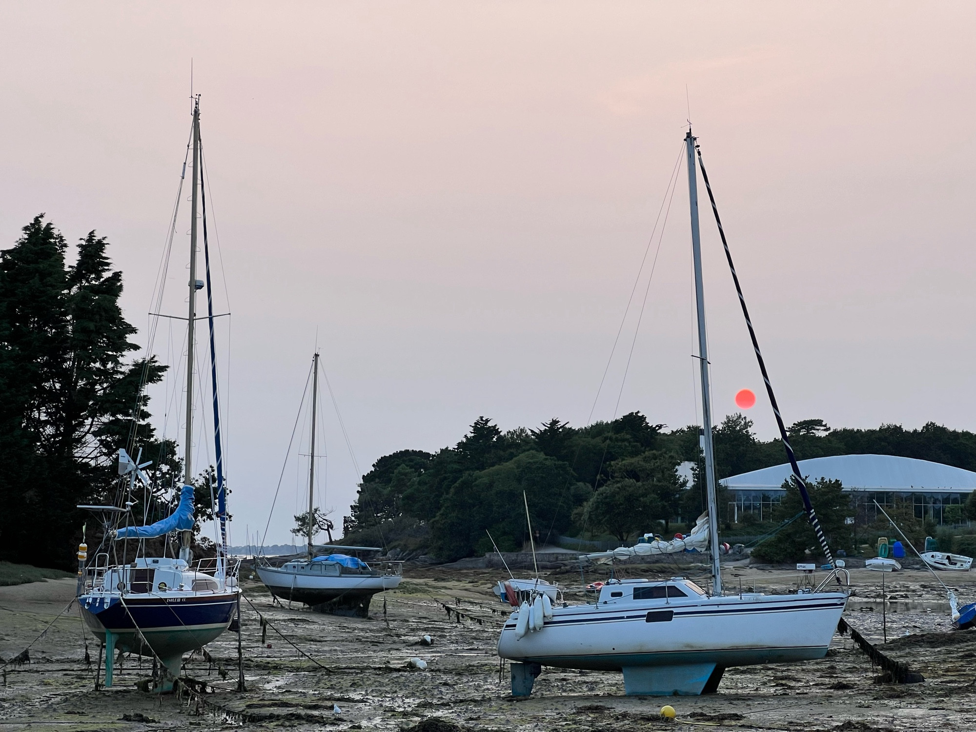 Voiliers à marée basse, un soleil couchant voilé apparaît comme un cercle rouge