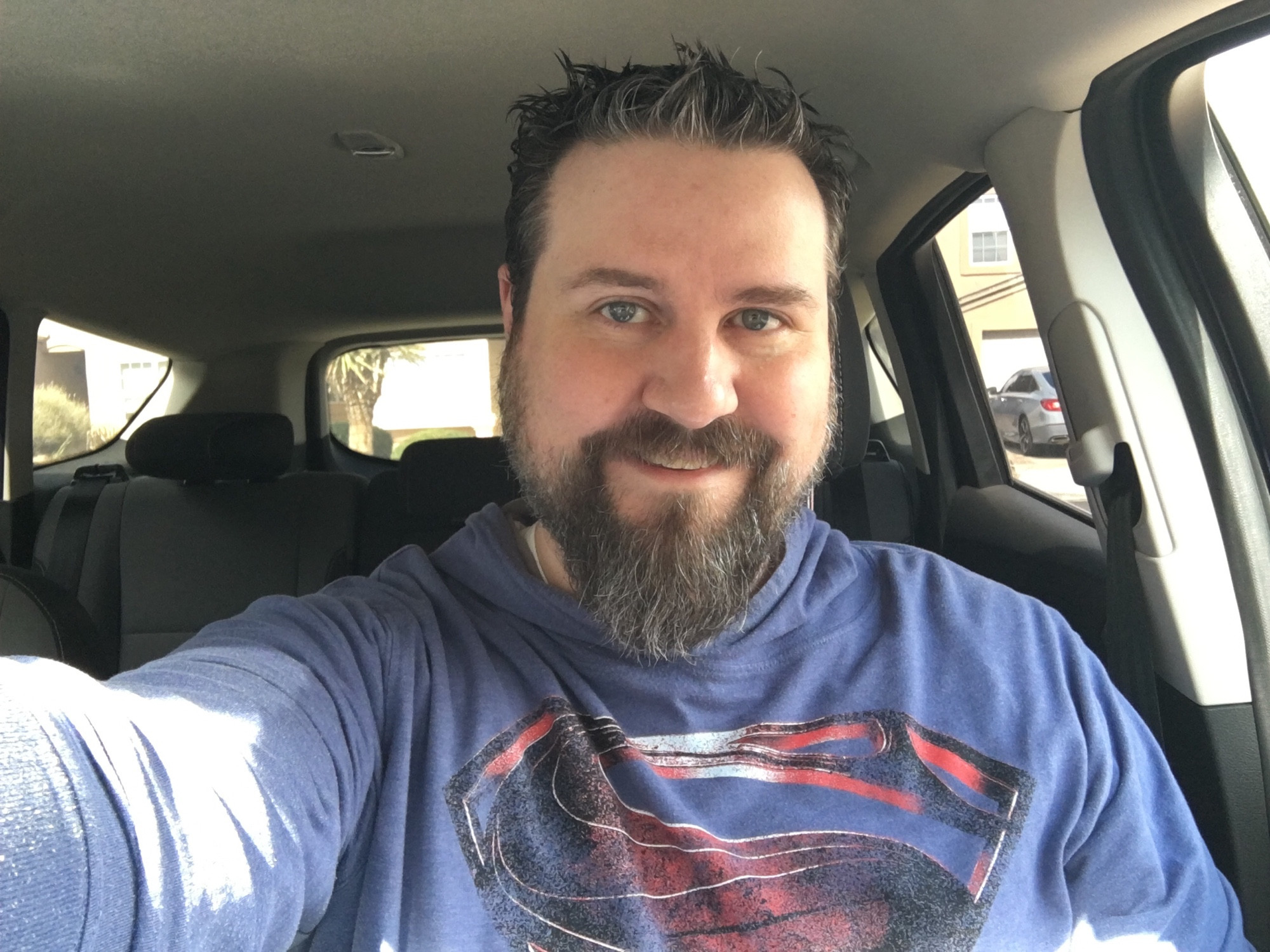 Pic of a bearded dude in his car, wearing a Superman hoodie.