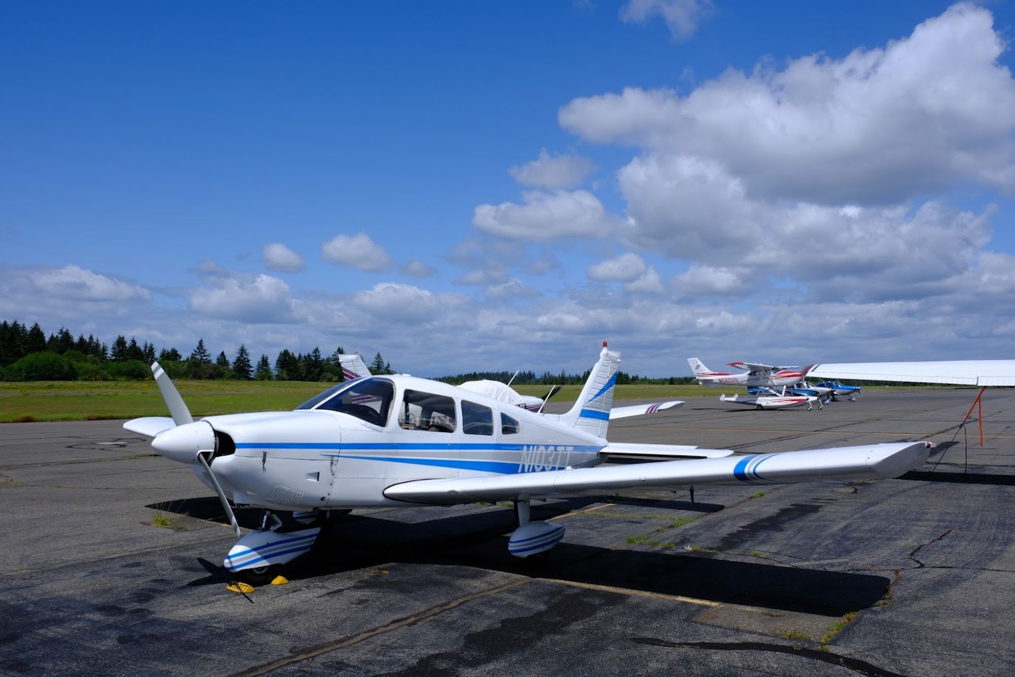 N103TT, a blue and white Piper Archer, sits chocked on the ramp at Tacoma Narrows airport under a blue sky with scattered clouds