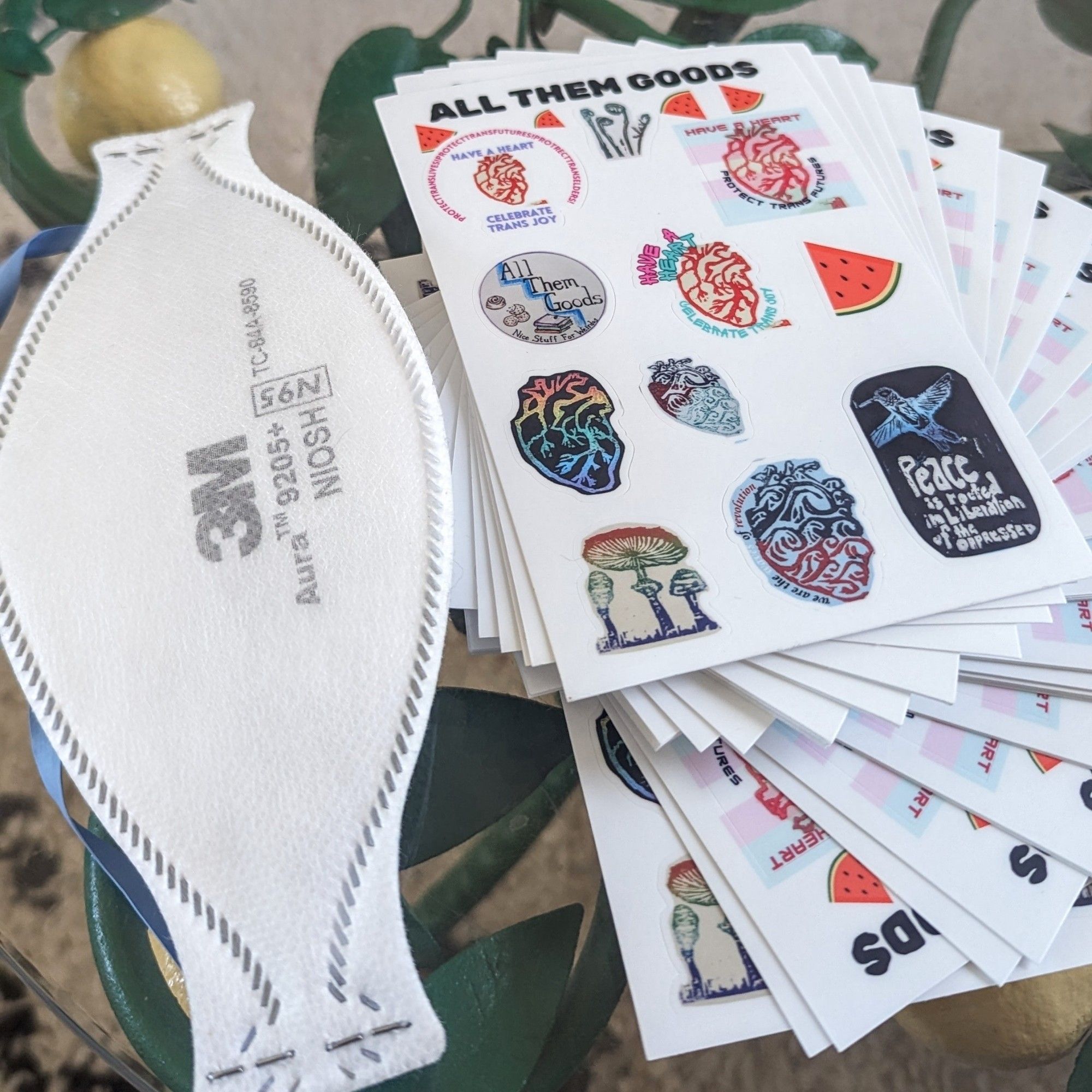 a 3M aura mask on a glass table next to a stack of sticker sheets fanned out beside them.