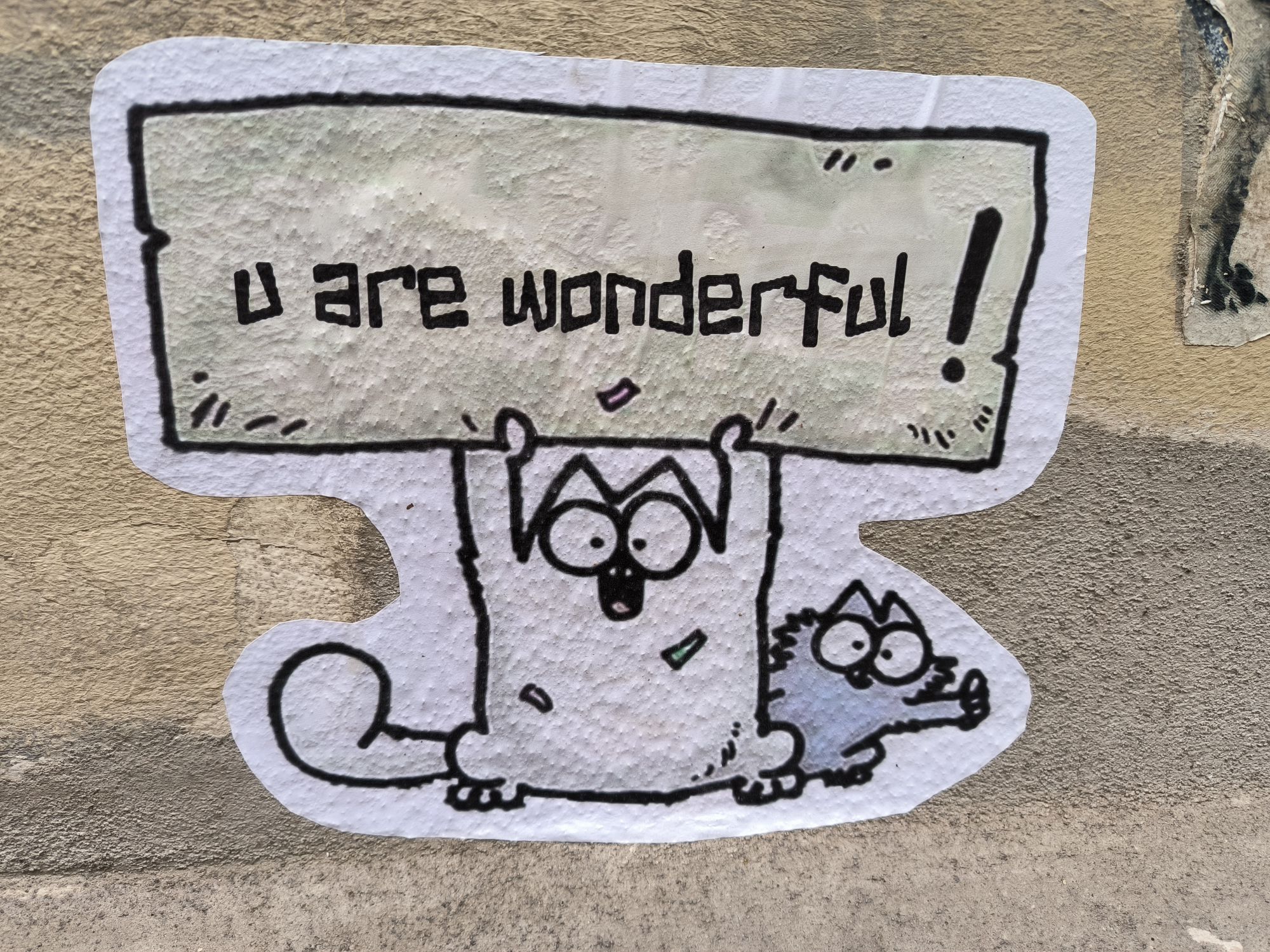 Simon's cat hält ein Schild mit der Aufschrift "u are wonderful!" hoch. Dahinter schaut eine kleine Katze mit hochgestrecktem Daumen hervor.