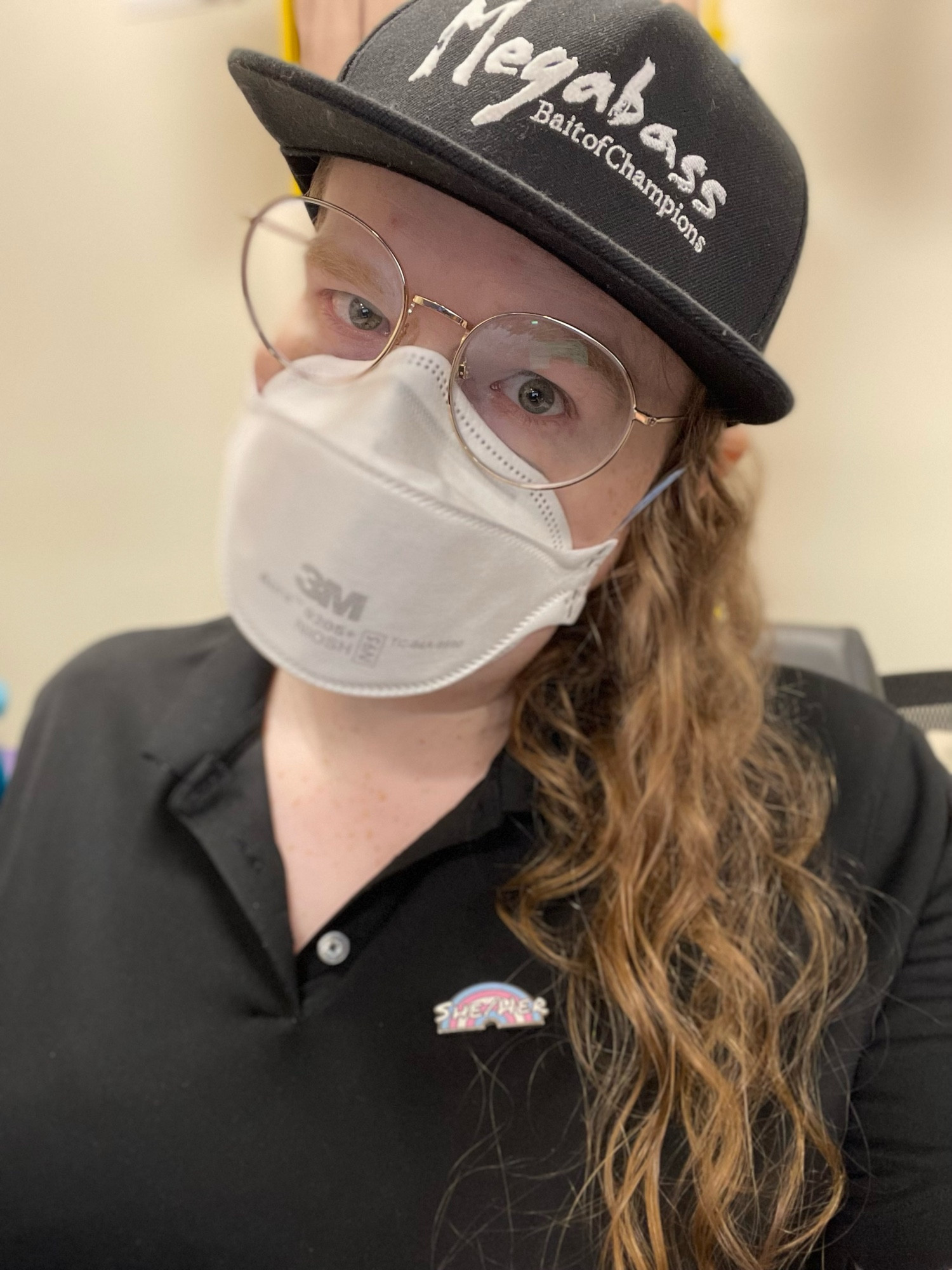 viola girlthing in its work shirt, black megabass hat, and she/her pronoun pins, which are not its pronouns but are the worksona pronouns