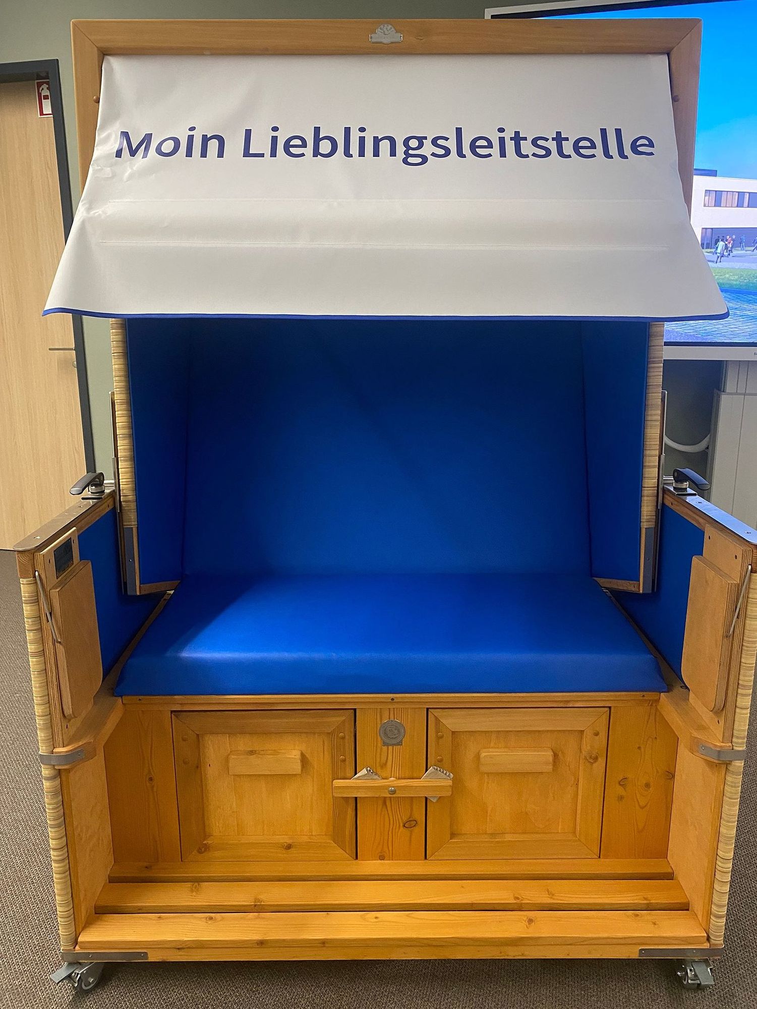 Strandkorb mit blauer Sitzfläche und Schriftzug "Moin Lieblingsleitstelle" auf dem Schirm.