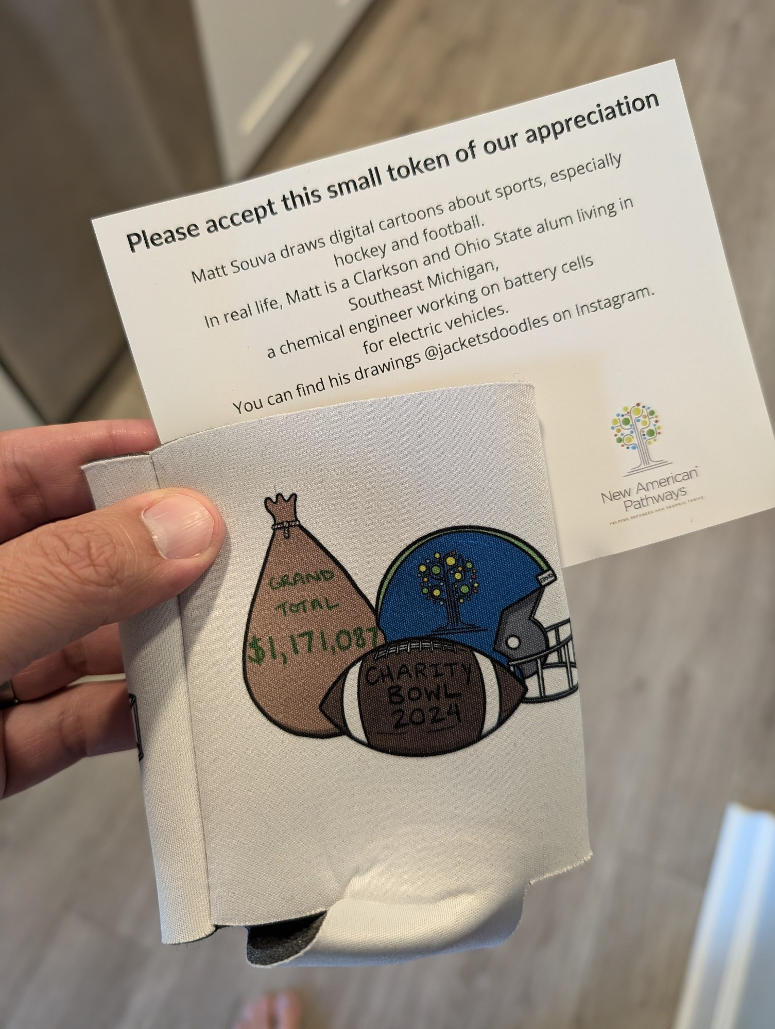 Pictured is a limited edition can koozie, celebrating the $1,171,087 raised by the Shutdown Fullcast's Charitibundi Bowl fundraiser for New American Pathways, along with a note from the designer. Not bad for a niche podcast. The koozie has a sack of money, a football, and a football helmet on it.