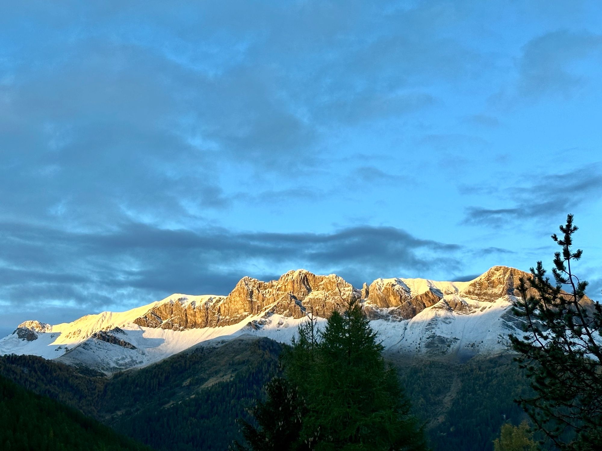 Une photo de montagnes enneigées au lever du soleil, sous un ciel bleu avec quelques nuages.