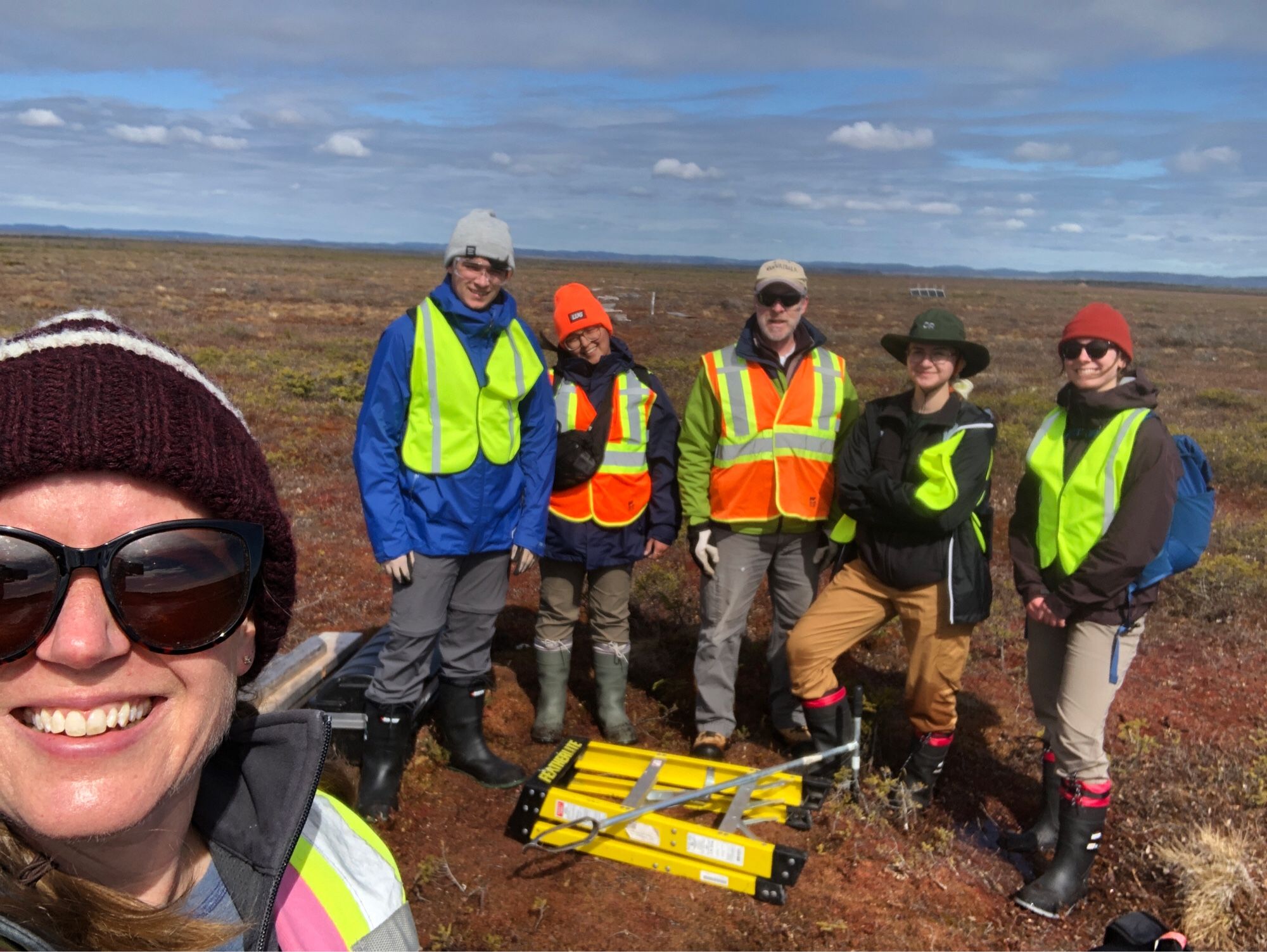 Maria Strack smiling in the foreground with a group of researchers in high visibility vests standing in a bog.