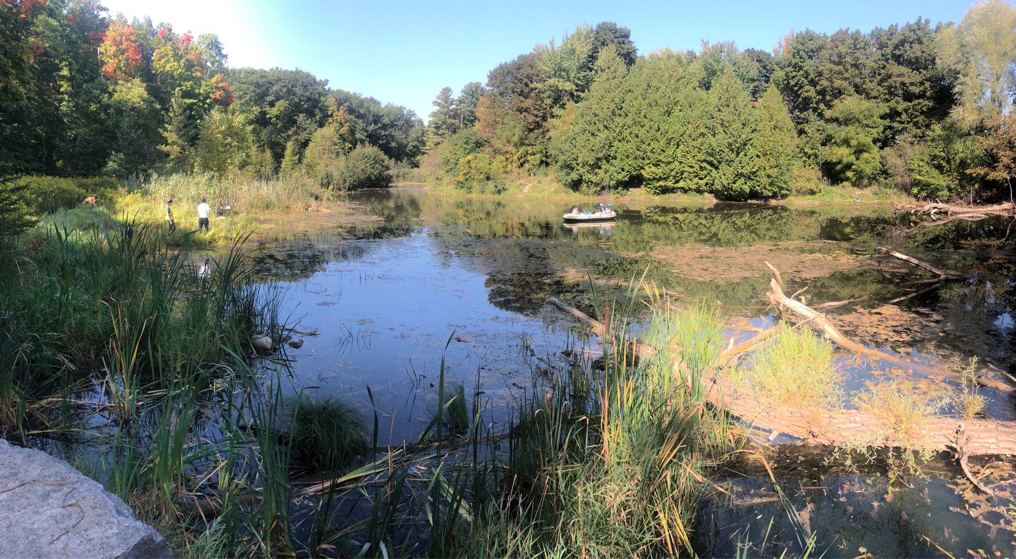 A boat with two researchers sits the the middle of a pond while additional researchers with laser sensors work on either shore.