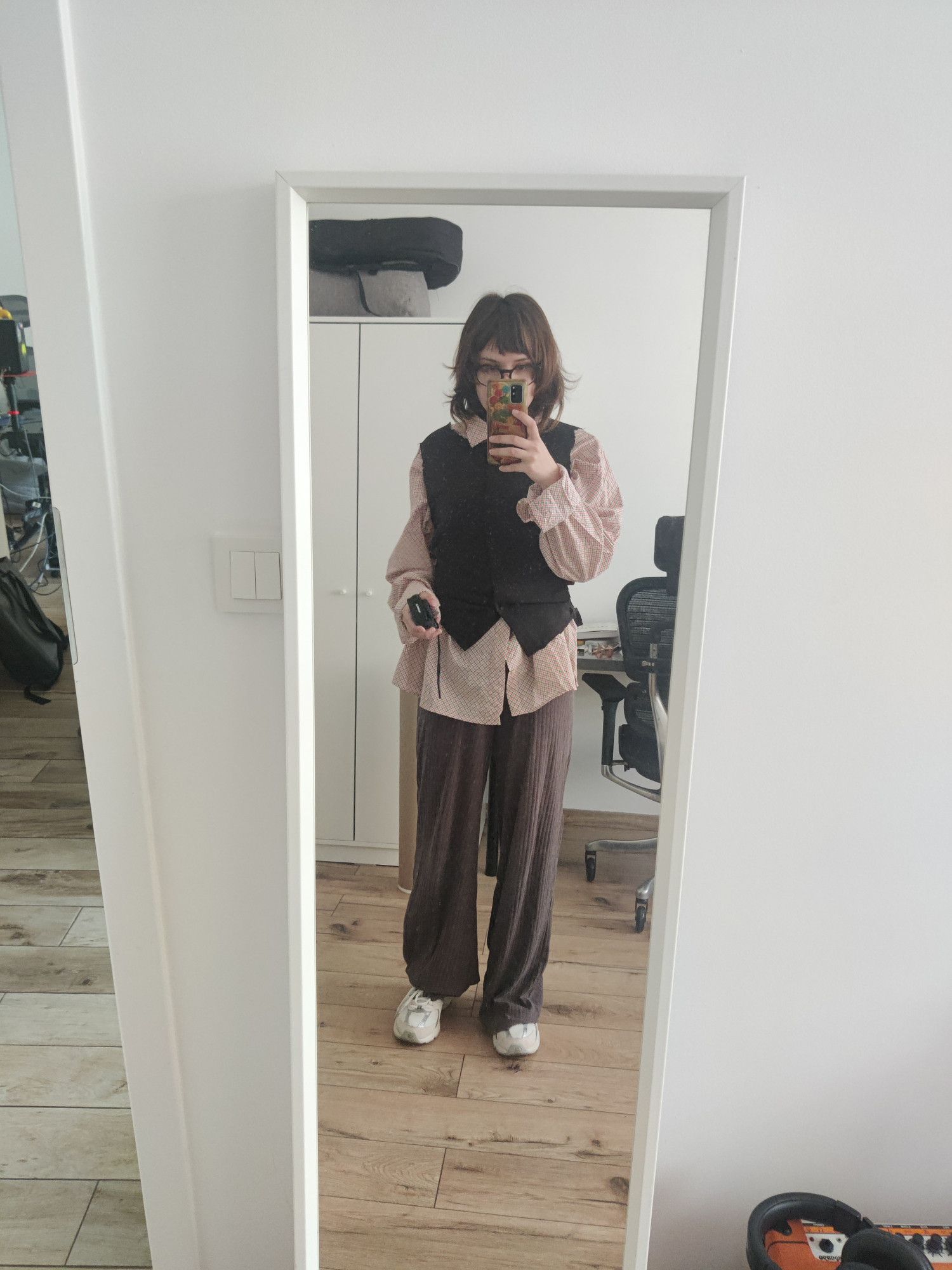 an image of a trans man wearing loose brown pants, a pink shirt and a black vest