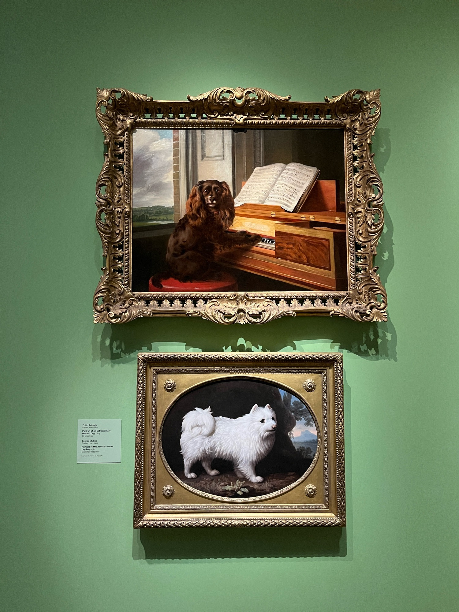 Two oil paintings of dogs in fancy frames, the top one is the piano-playing dog.