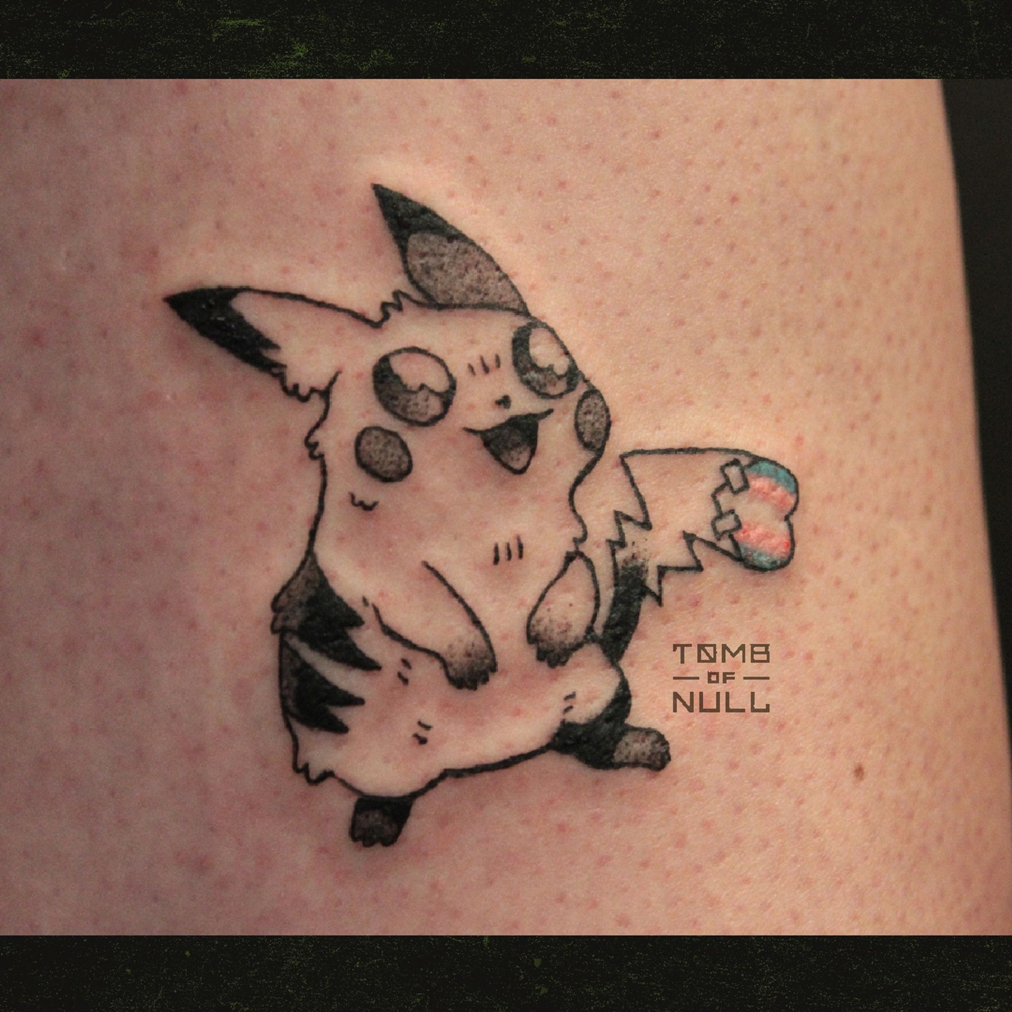 A fresh tattoo of a pikachu. Her tail has a heat-shaped flag affixed to her tail, sporting the trans pride flag. Her expression is cute.