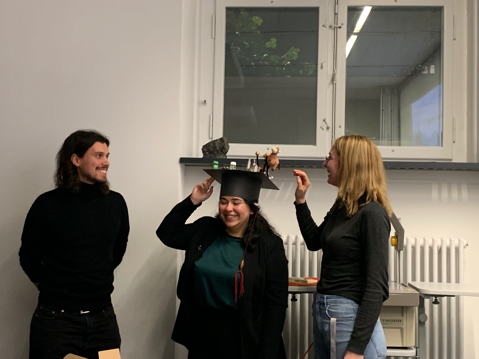 PhD student receiving the traditional PhD hat with decorations of a cow, lake sediment, and other.