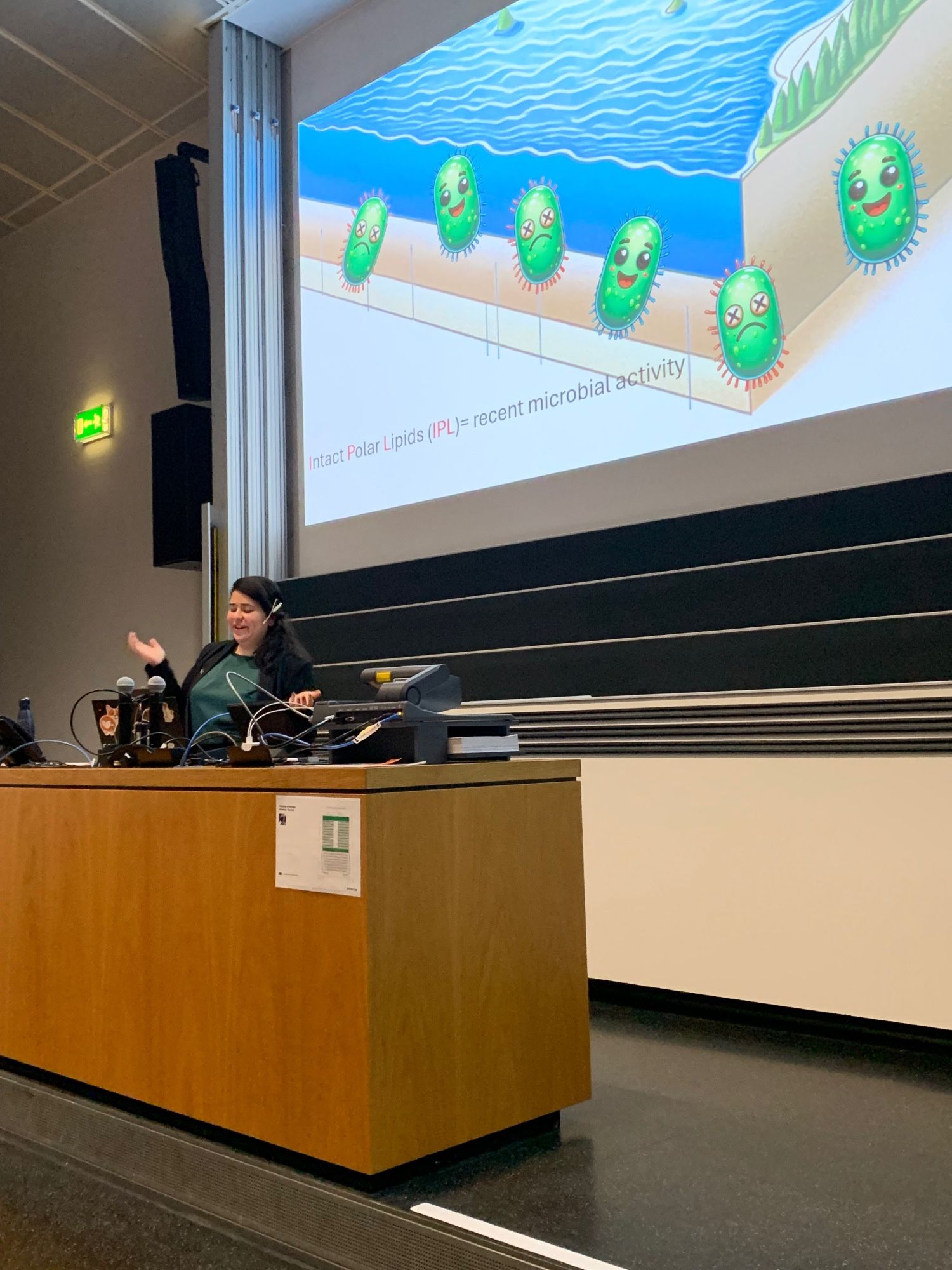 PhD student standing in front of a slide with cartoons of lake bacteria, and the words ‘intact polar lipids’.