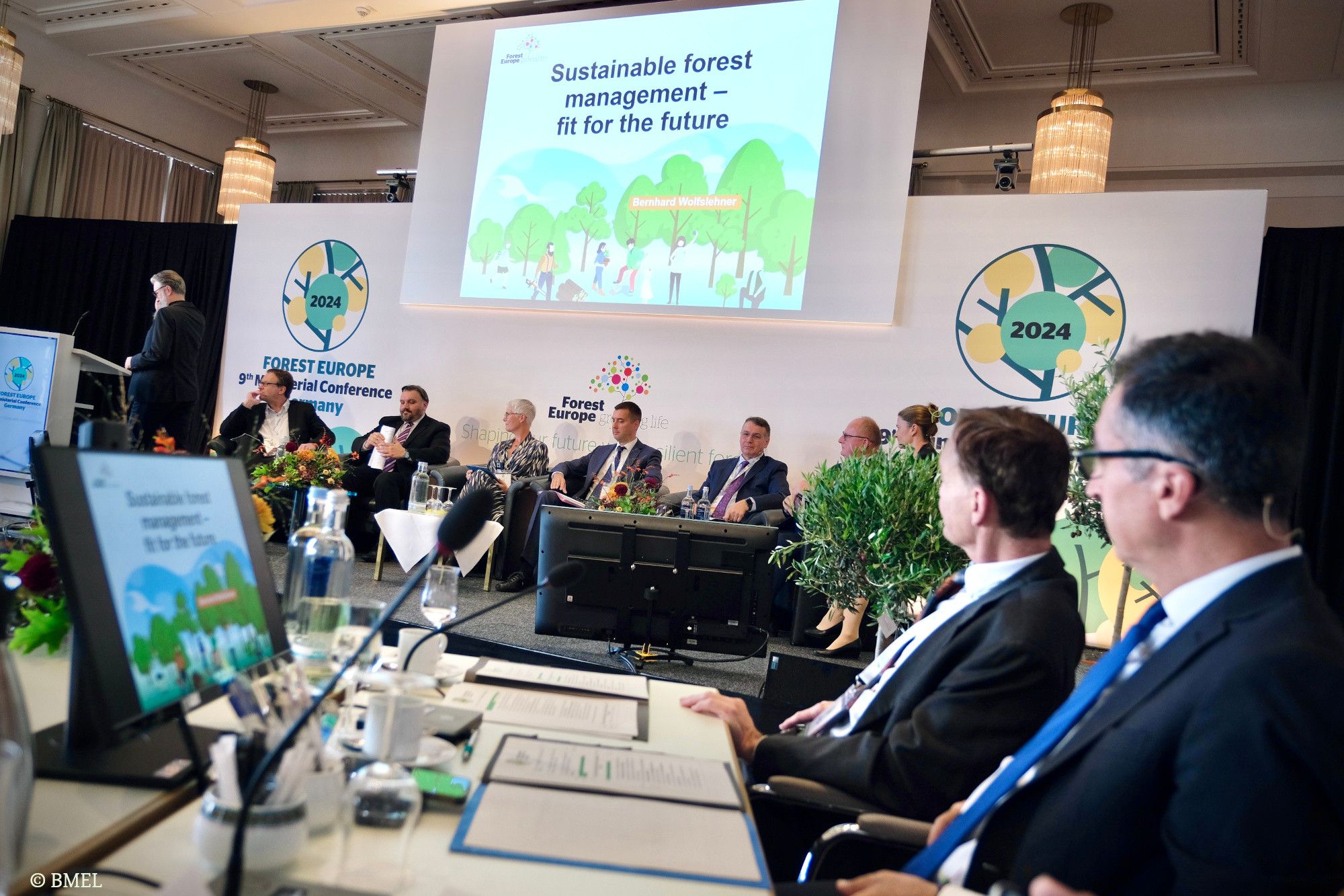 Die Podiumsdiskussion auf der Bühne. Im Hintergrund die Logos von Forest-Europe. Im Vordergrund Bundesminister Cem Özdemir.