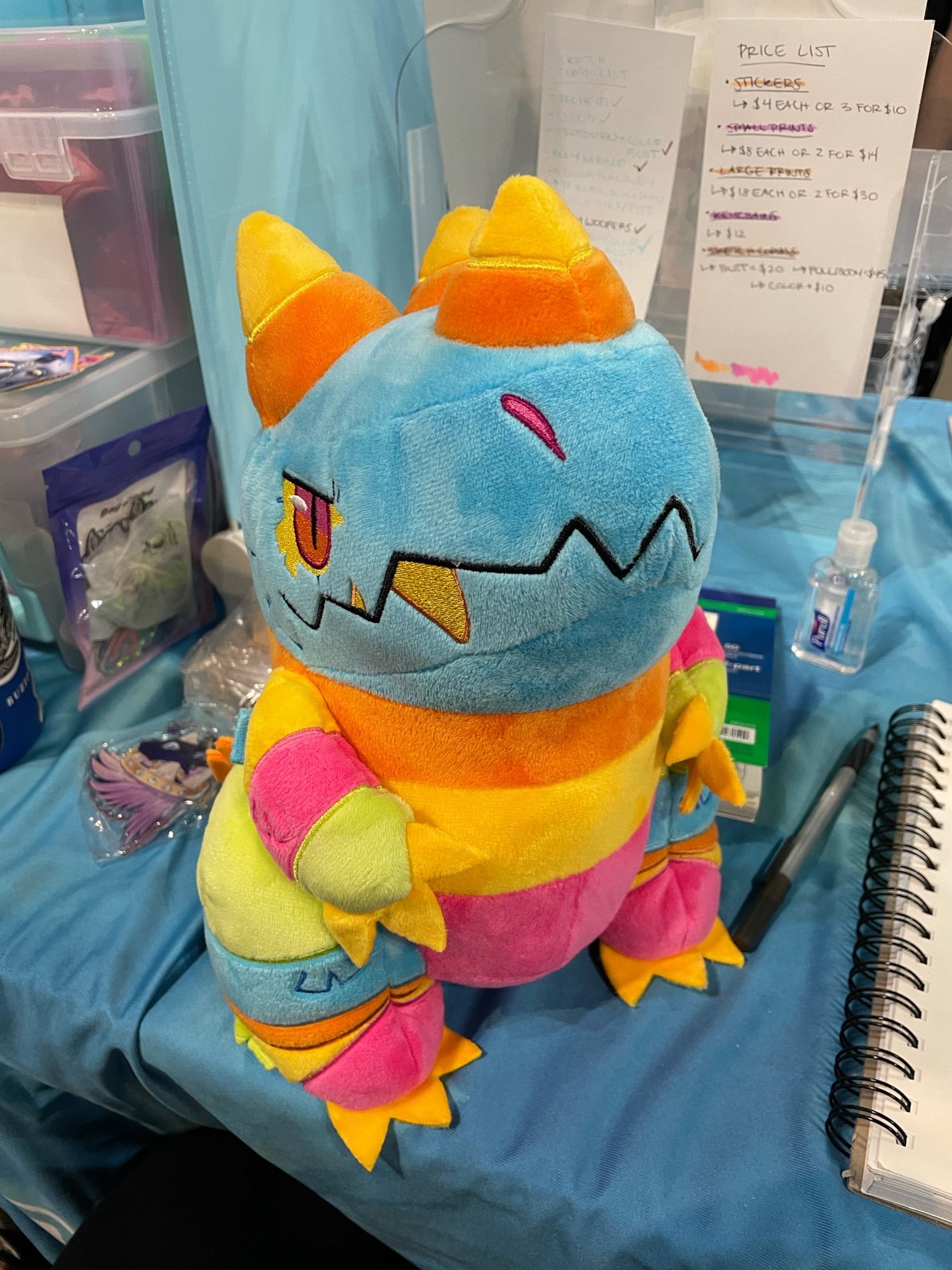 Pinata kaiju plush sittin on a blue tablecloth, there is work clutter about

#kaiju #furry #furcon #anotherfurrycon