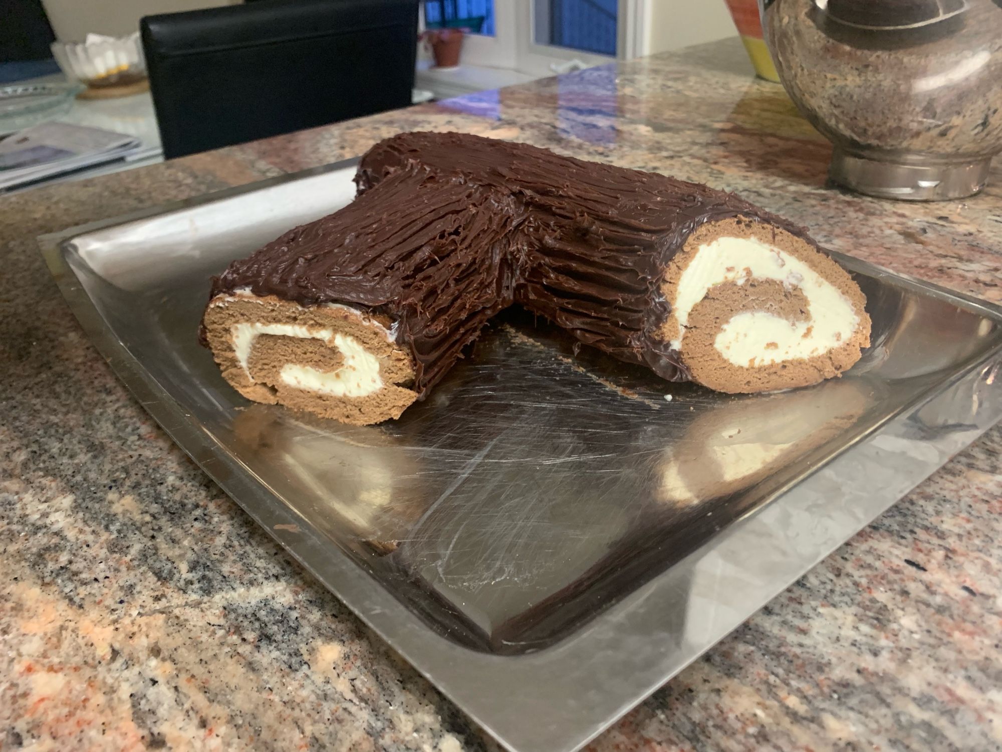 Yule log on a stainless steel platter. Made of cake, rolled with cream cheese whipped cream, frosted with a chocolate ganache scored to look like wood grain.