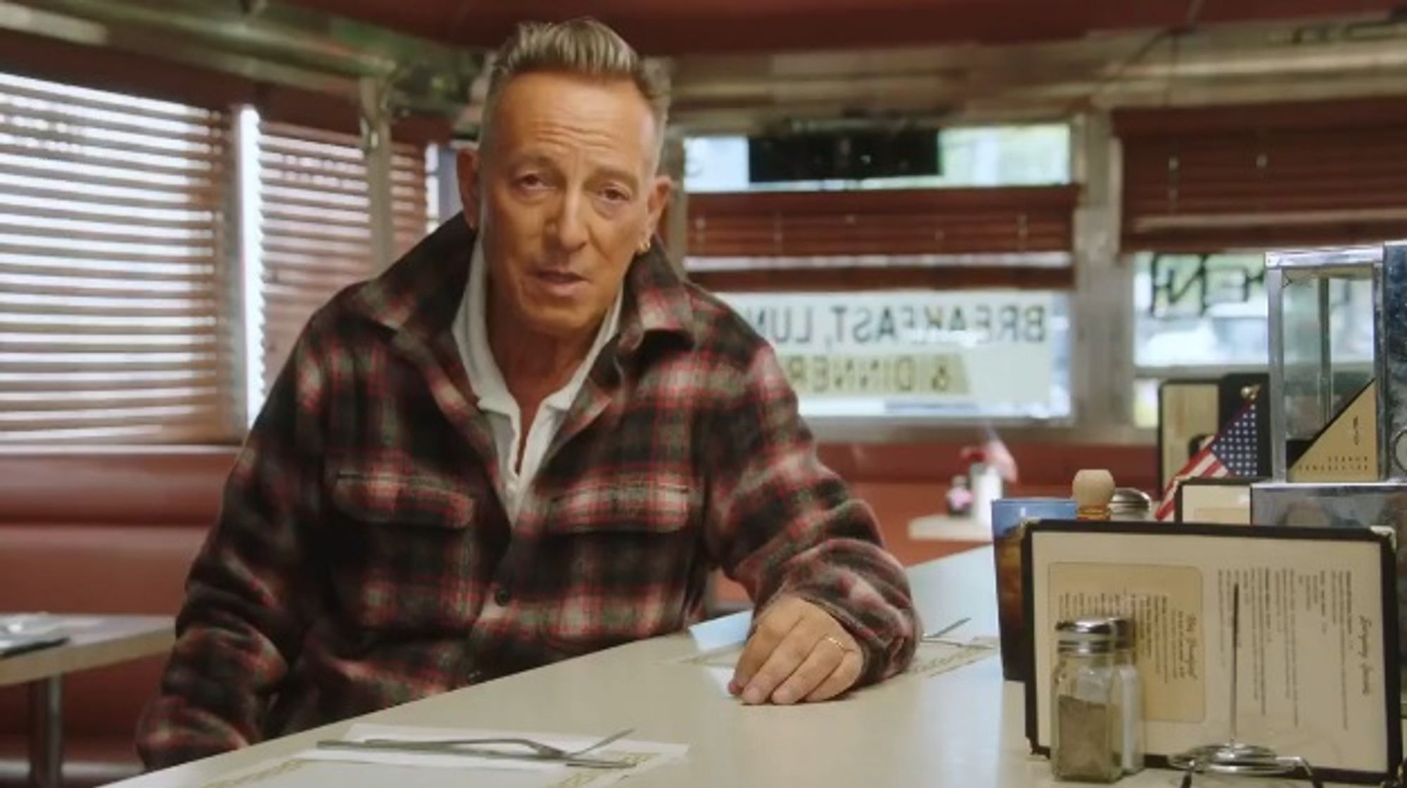 Bruce Springsteen sitting at the counter of a diner, addressing the camera.