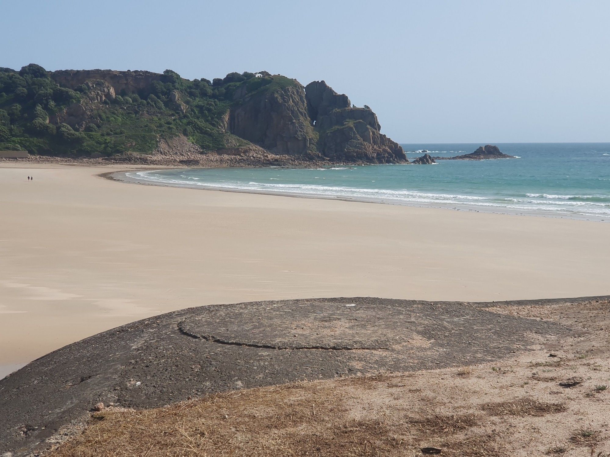 In the foreground a concrete German Bunker, in the distance a granite headland and cave 