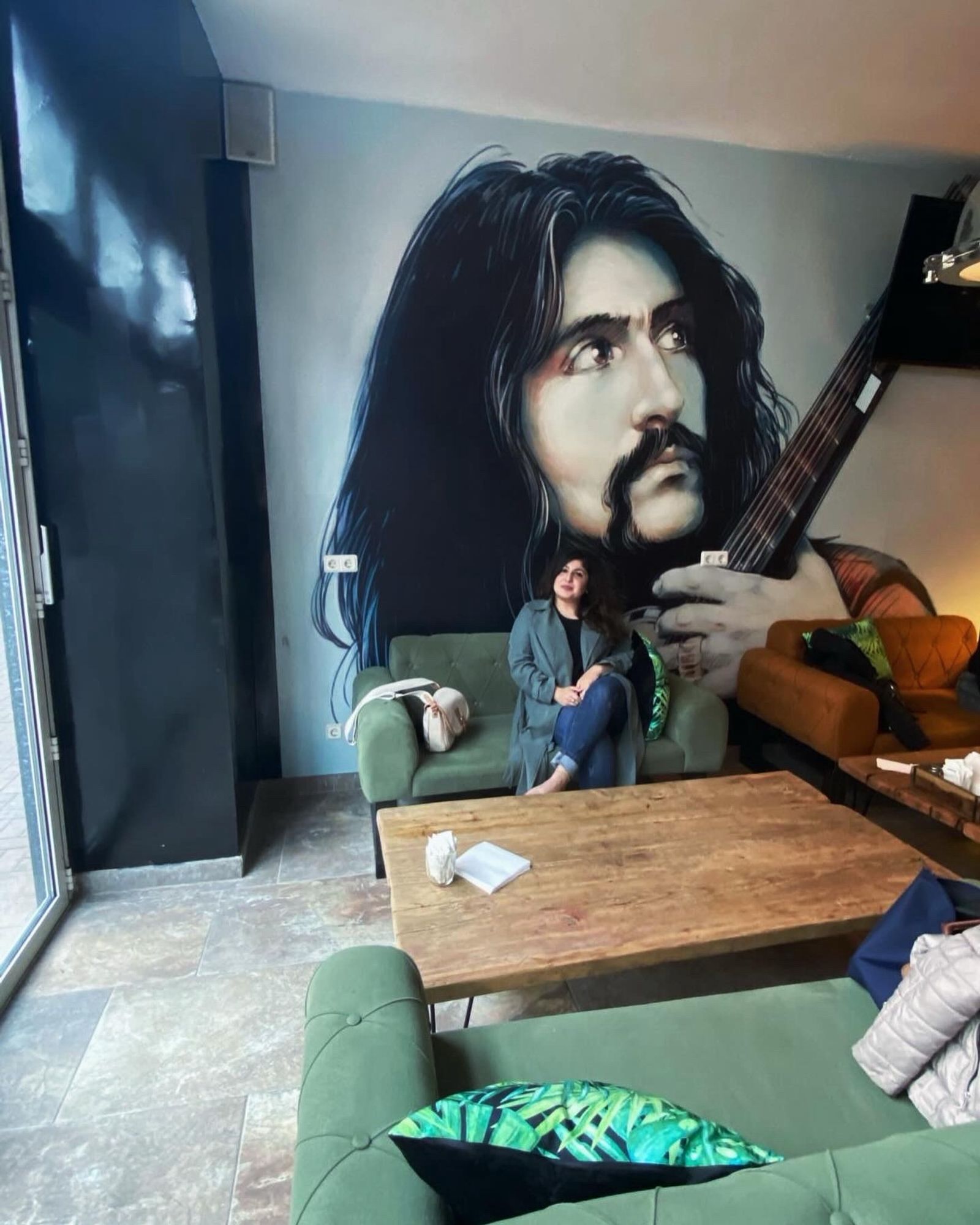 Ich, wie ich auf einem Sofa in einem Café sitze. Im Hintergrund ist auf einer Wand das Bild des berühmten Sängers Baris Manco zu sehen.