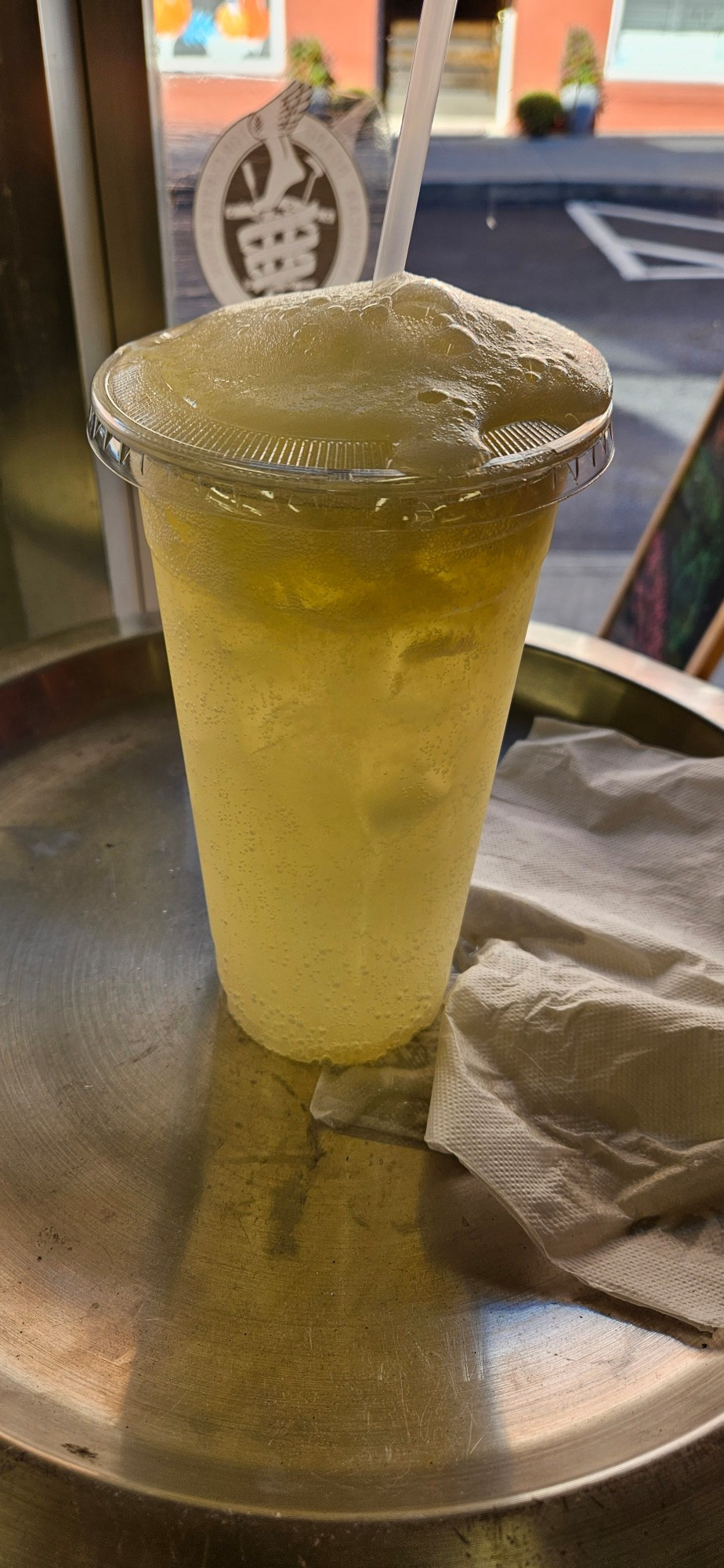 Large plastic cup with a lemon drink with foam spilling out the top.