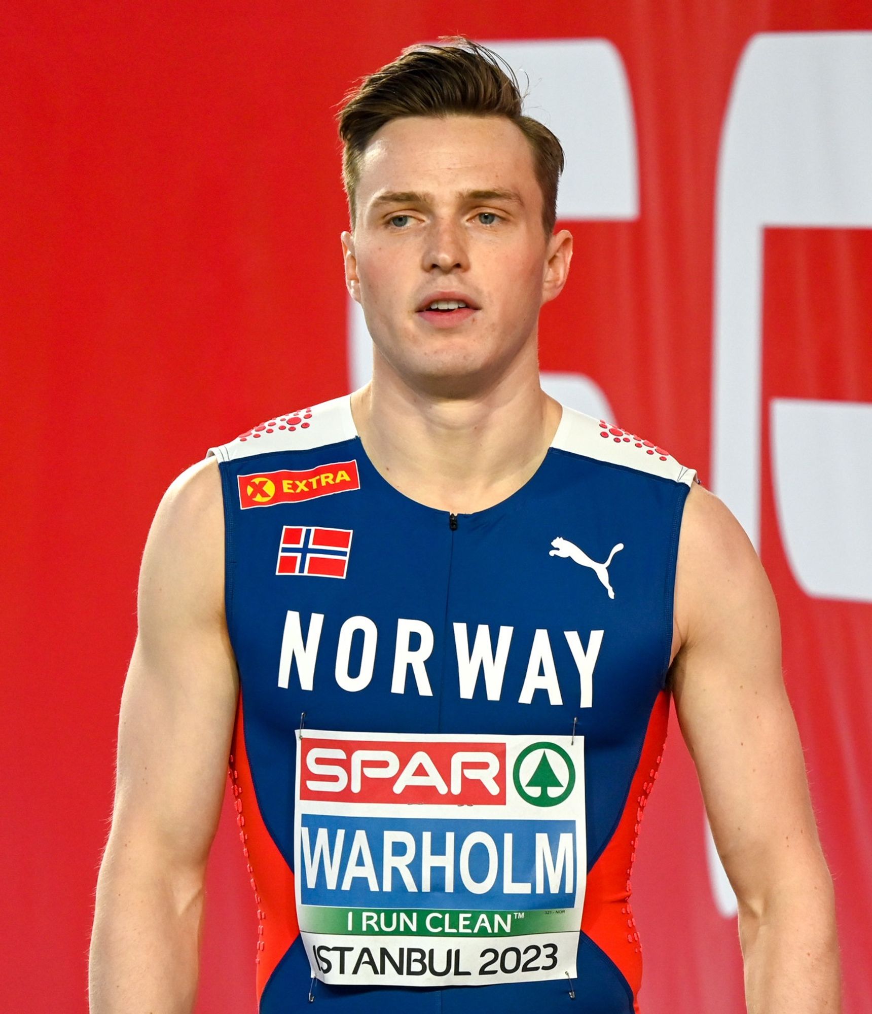 Karsten Warholm in his Norway track uniform. He has blond hair and blue eyes and has a haircut that looks a bit like the kids wore it in Nazi Germany